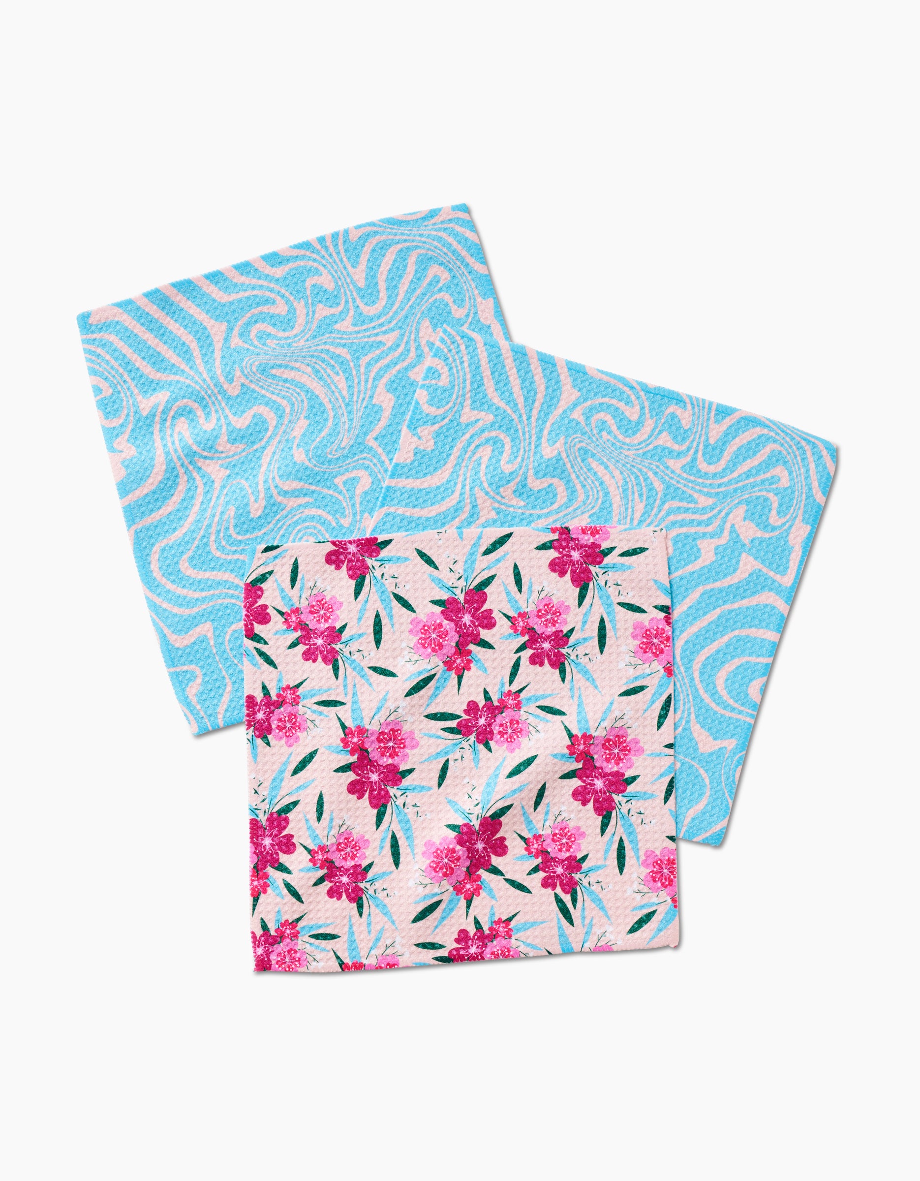 The GEOMETRY Sending Love Dishcloth Set includes two super-absorbent Geoweave cloths: one with a blue and white swirl design, the other featuring pink flowers and green leaves on a white background.