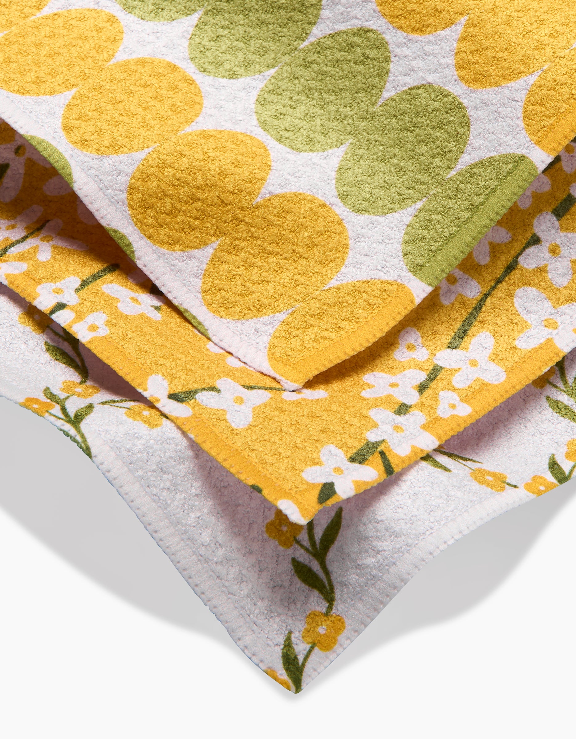 Two Kayla Ann “Signs of Springtime” towels are stacked: the top in Geoweave shows bold yellow and green circles, while the bottom has a yellow border with small white flowers and green leaves.