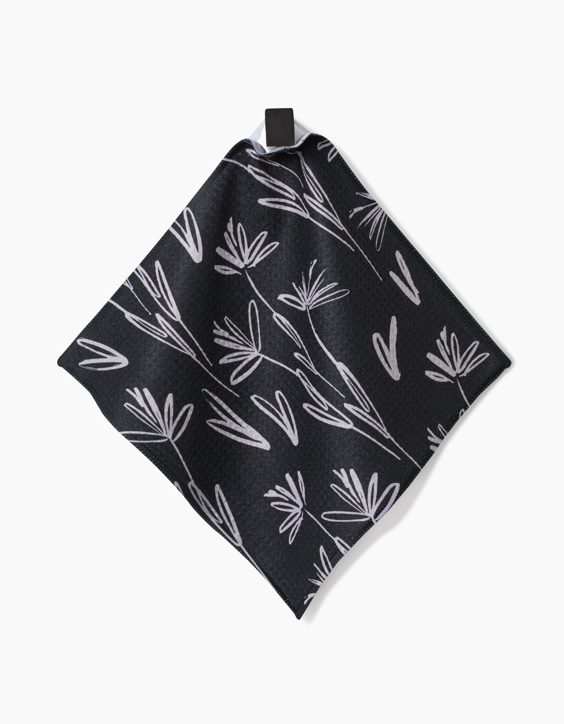 The Sketchbook Dusk by Toboggan Avenue is a black Geoweave fabric square dishcloth featuring a white floral pattern and a black hanging loop, shown against a plain white background.