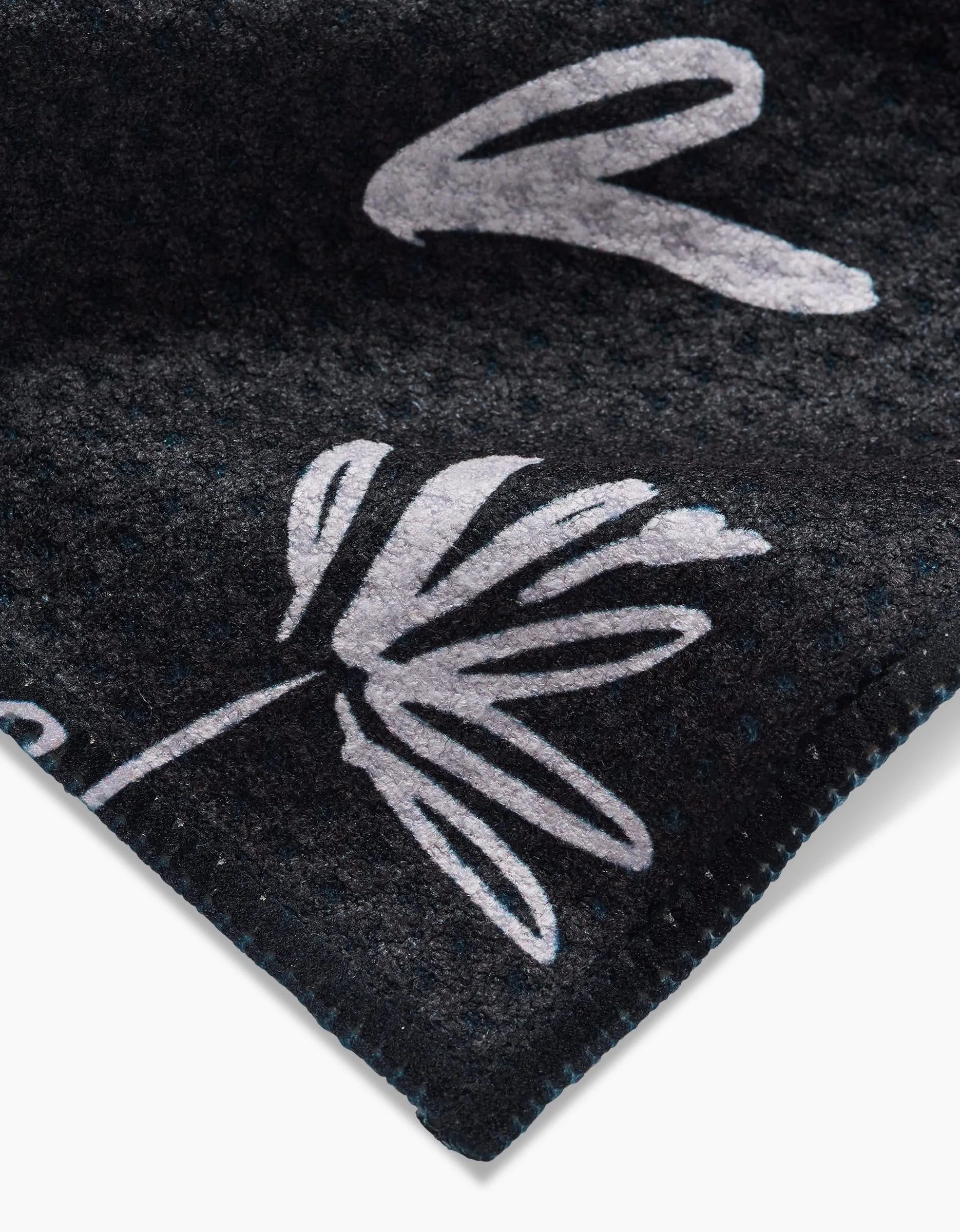 A close-up of the Toboggan Avenue Sketchbook Dusk dishcloth, showcasing dark Geoweave fabric with a white abstract floral pattern and neatly stitched edges.