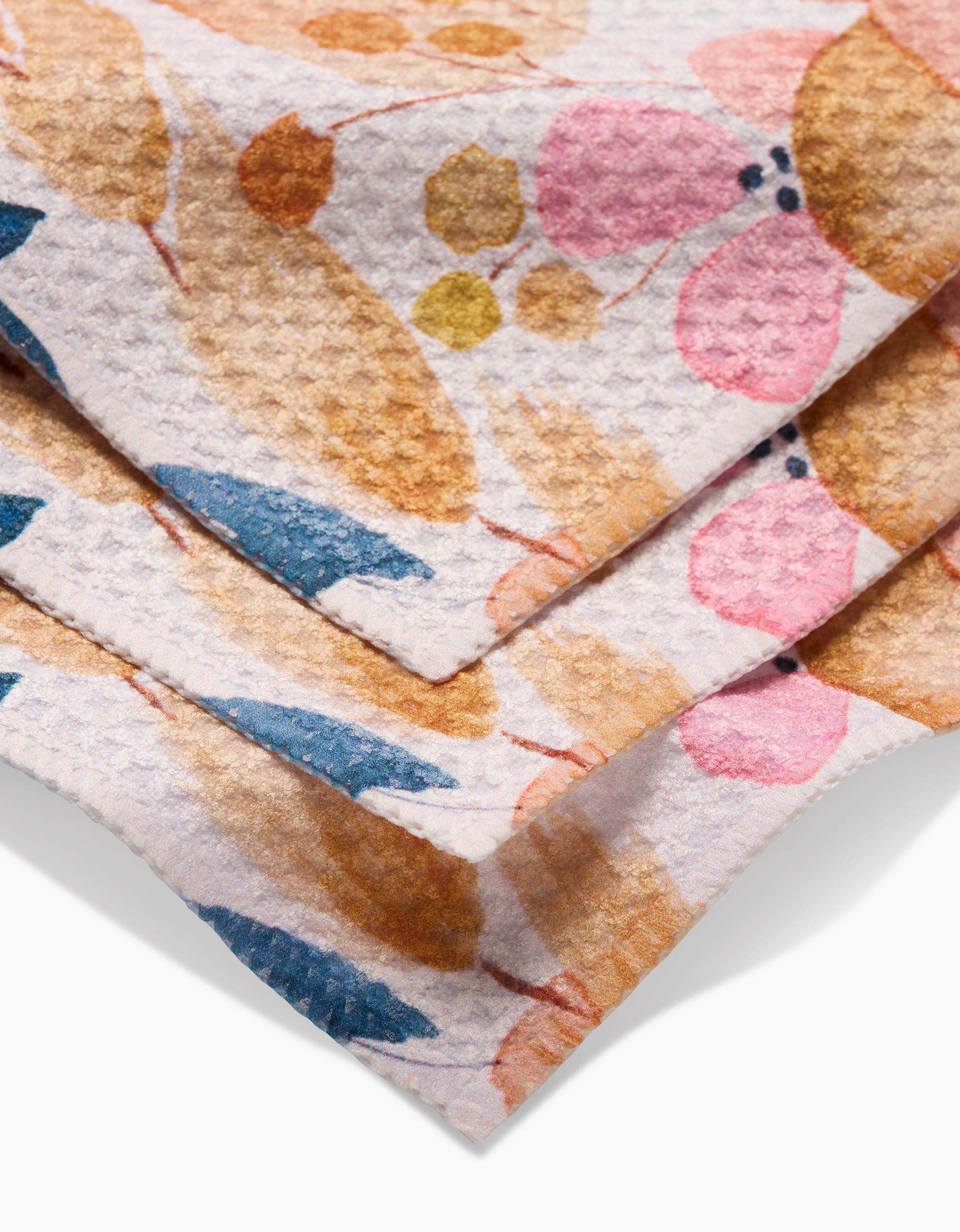 A close-up of GEOMETRYs Sleepy Fields dishcloths made from Geoweave fabric, showcasing a floral pattern with pink, blue, yellow, and brown leaves and flowers on a white background.