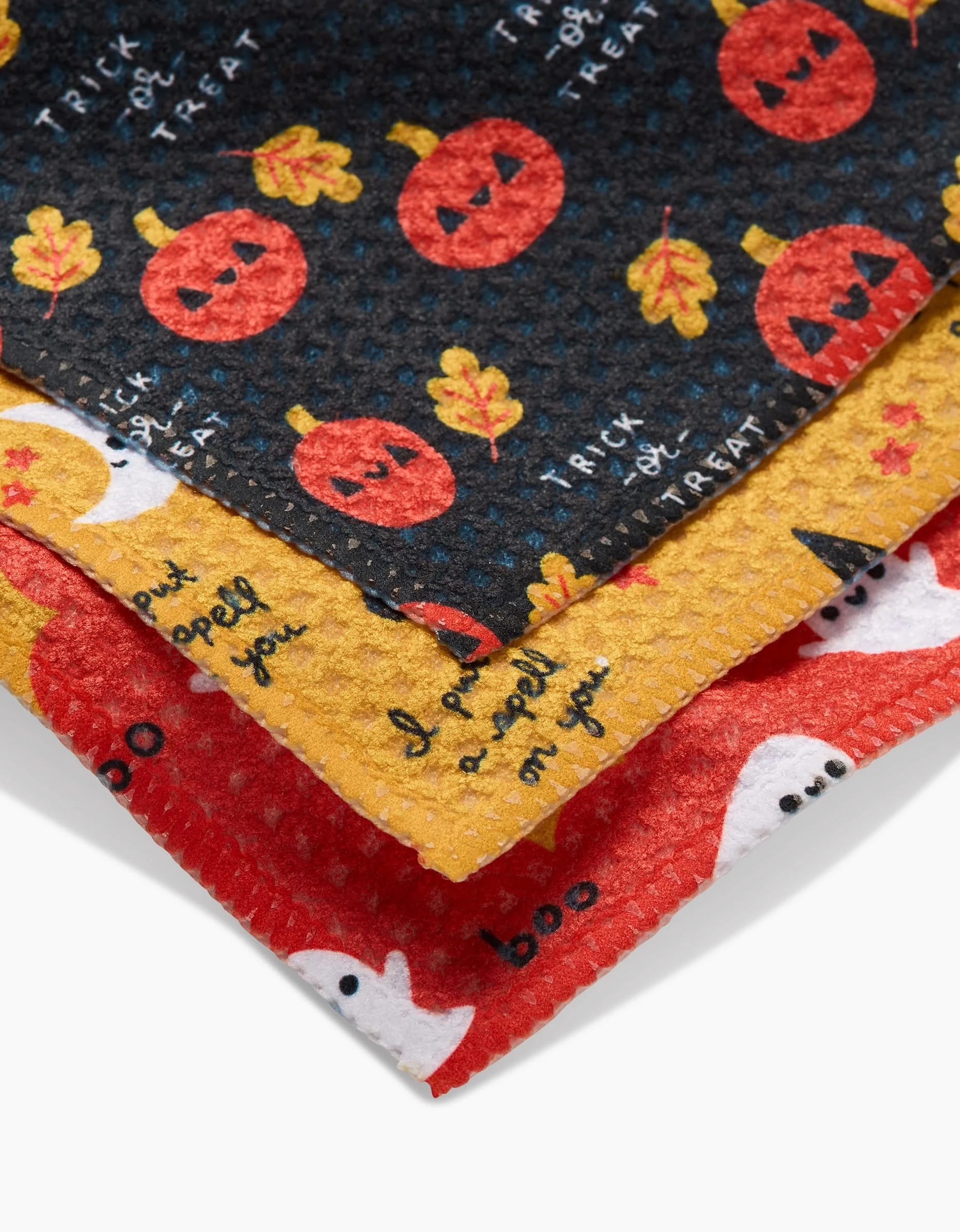 The Spooky Season set by Genna Blackburn includes three Halloween-themed Geoweave dishcloths—black with pumpkins and leaves, yellow with pumpkins and “I put a spell on you” text, and red with white ghosts and boo—made from recycled materials.