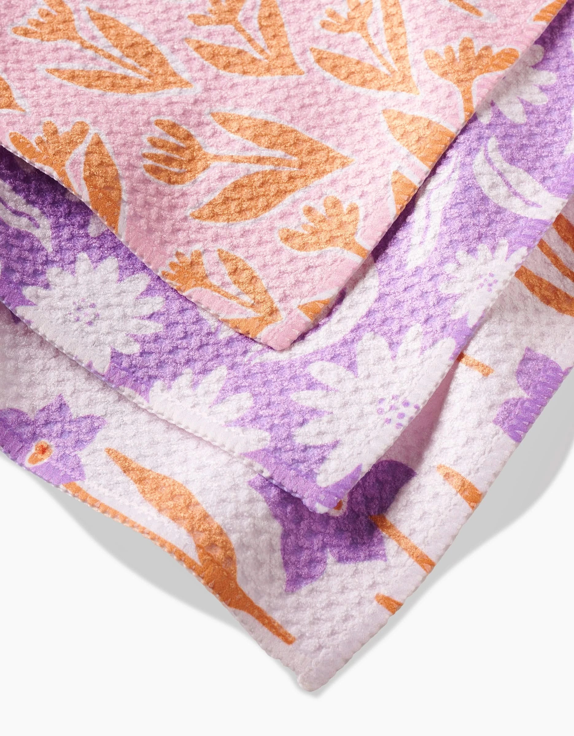 Three layered Kayla Ann Spring Flowers Geoweave dishcloths feature vibrant floral designs: pink with orange flowers on top, purple with white flowers in the middle, and white with purple and orange flowers at the bottom.