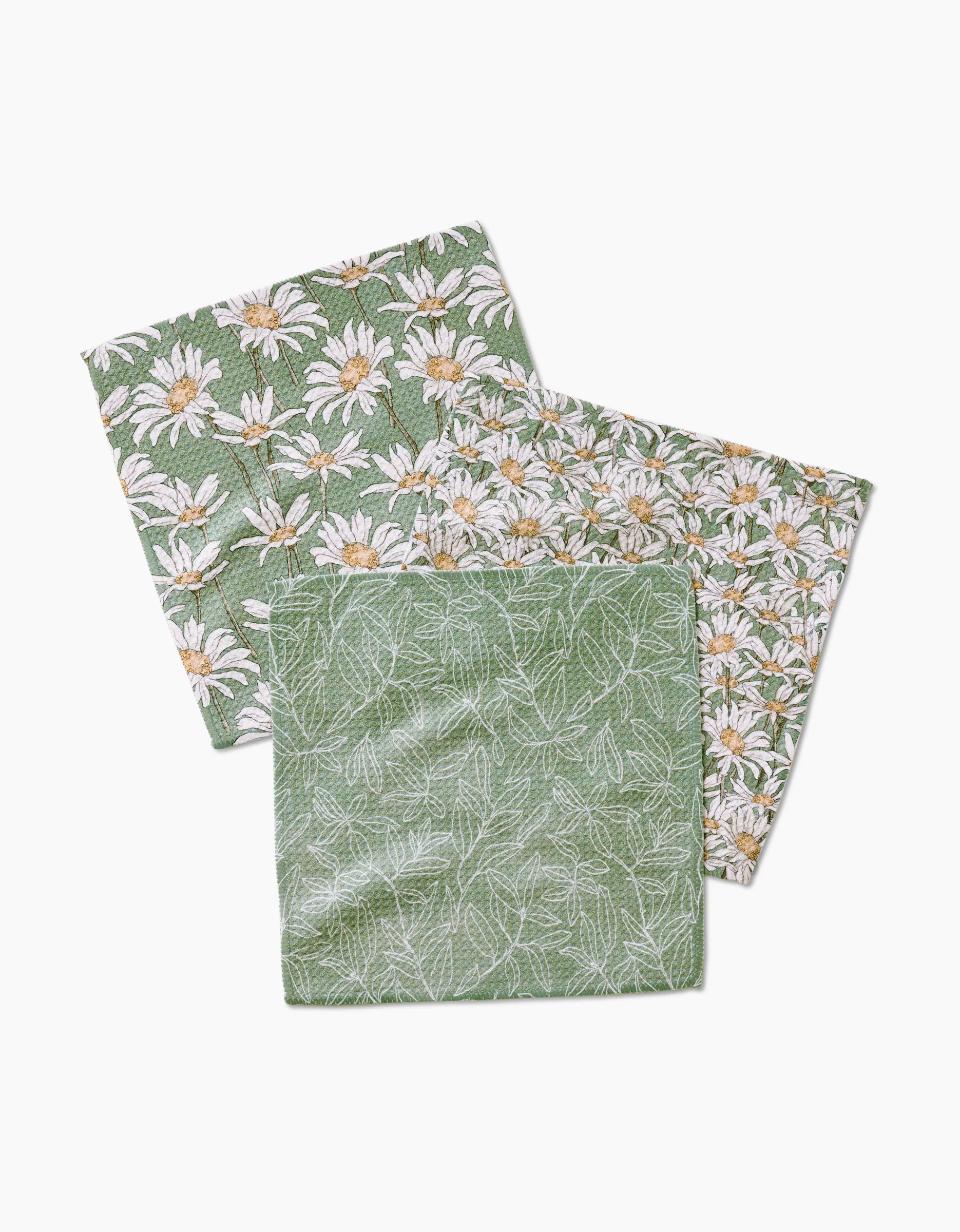 The Aubrey Fairchild Springtime set includes three green Geoweave cloth napkins: two have a white and yellow daisy floral print, and one features a subtle white leaf pattern—all on a crisp white background.