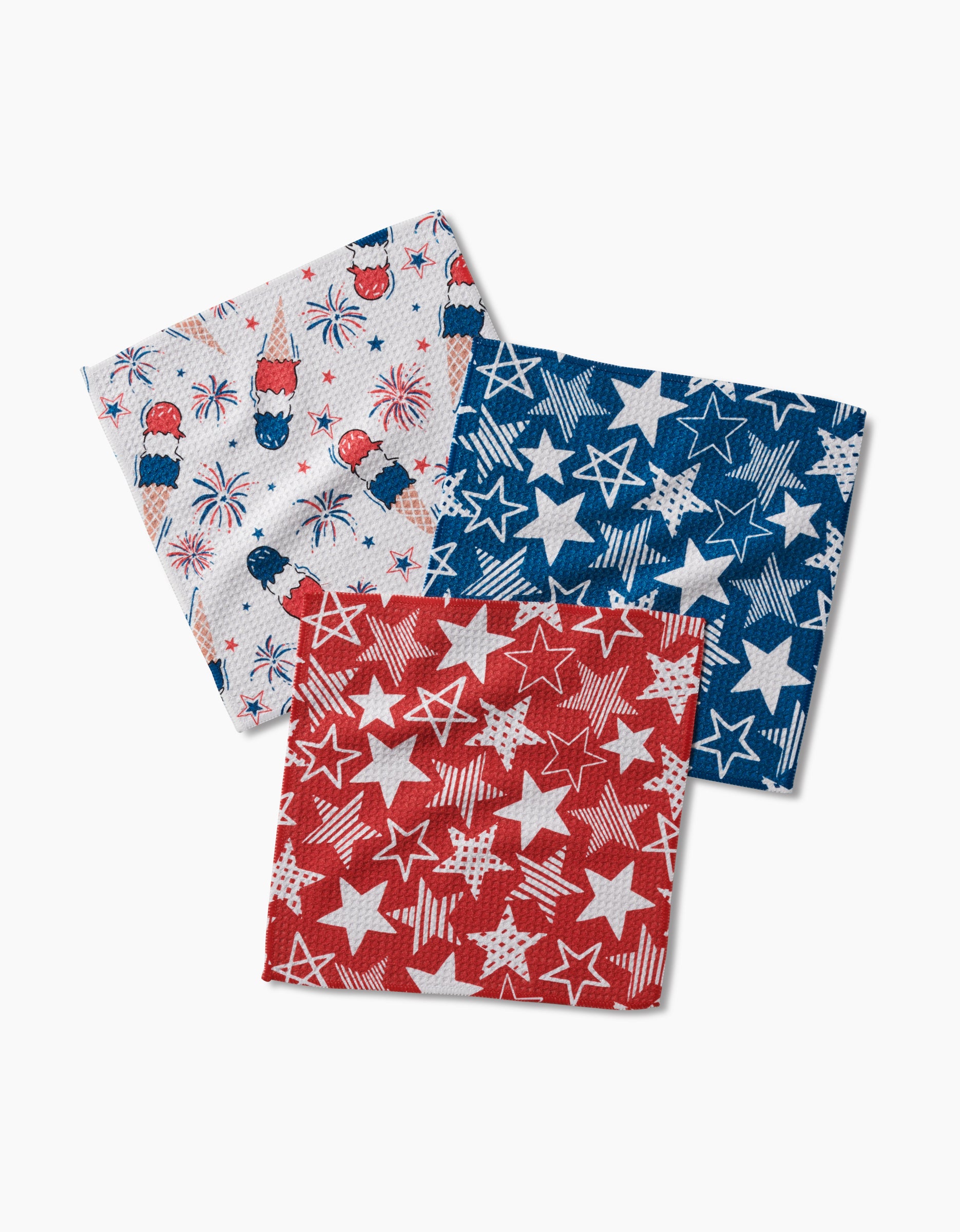 The Stars In Your Eyes set by Hufton Studio includes three recycled cloth napkins with patriotic designs: white with fireworks and rockets, blue with white stars, and red with white stars.