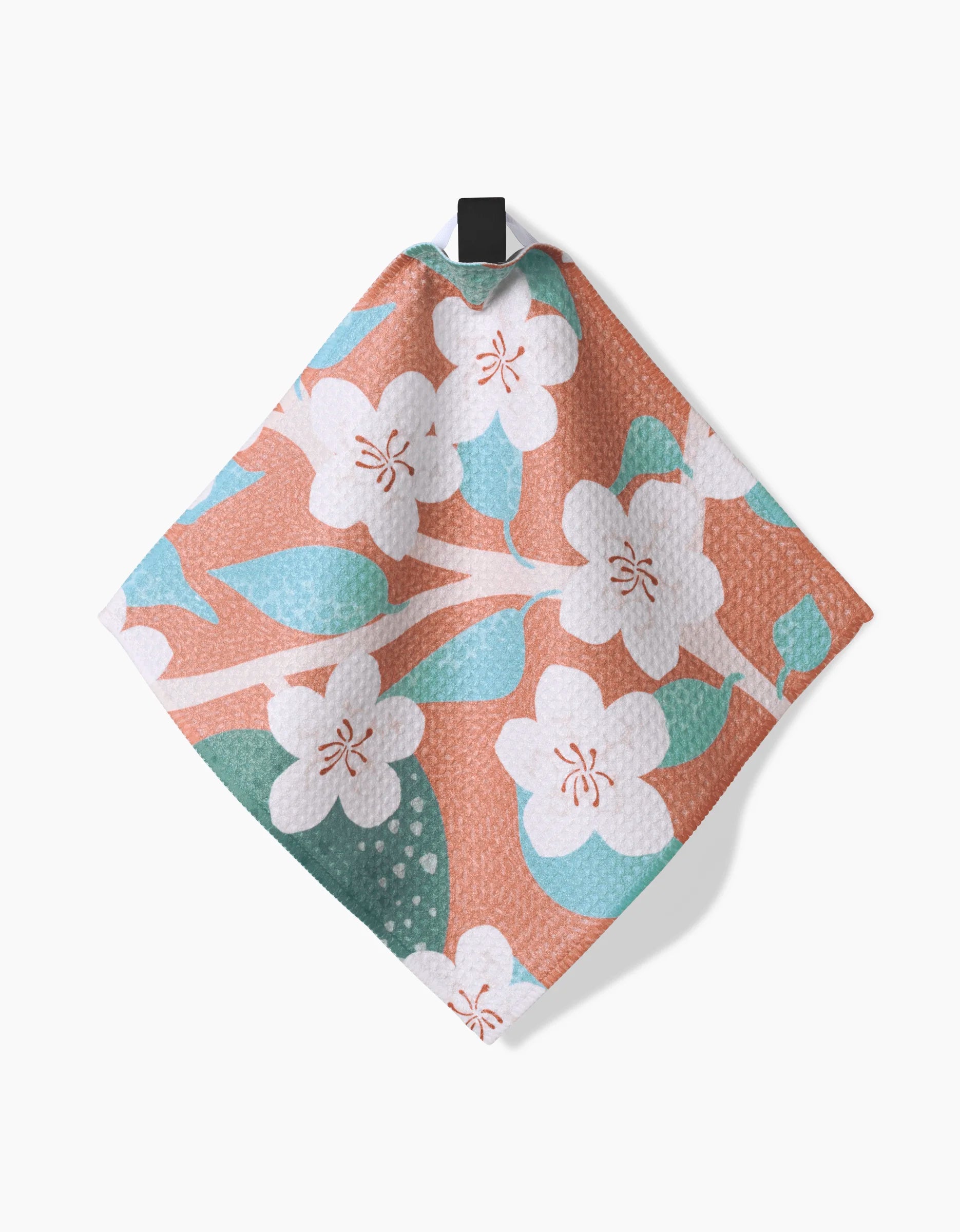The Julianne Haness State Flowers towel is crafted from textured Geoweave fabric and features white flowers, green leaves, and blue accents on a pinkish-coral background, hanging from a black loop.