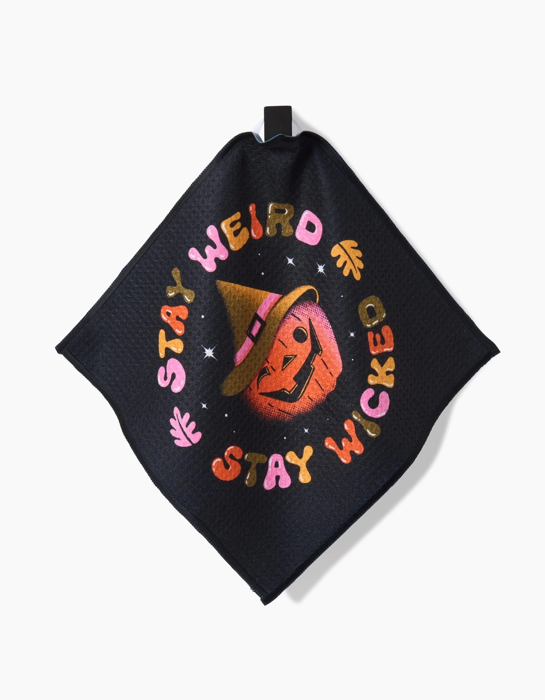 The “Stay Weird Stay Wicked” dishtowel by Megan Roy is a black cloth towel with a Halloween jack-o-lantern in a witch hat, colorful spooky text, and stars—crafted from recycled materials.