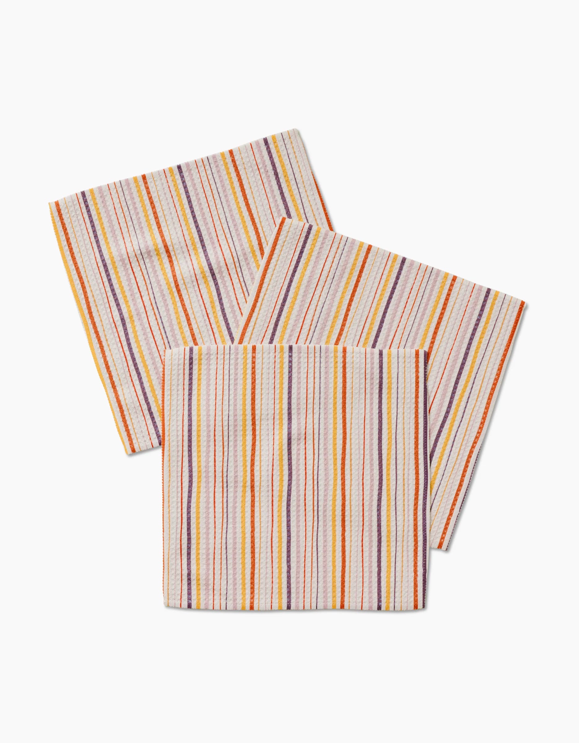 The GEOMETRY Stripe Season features three overlapping, super-absorbent cloth napkins with orange, yellow, and purple stripes on white—perfect for everyday use.