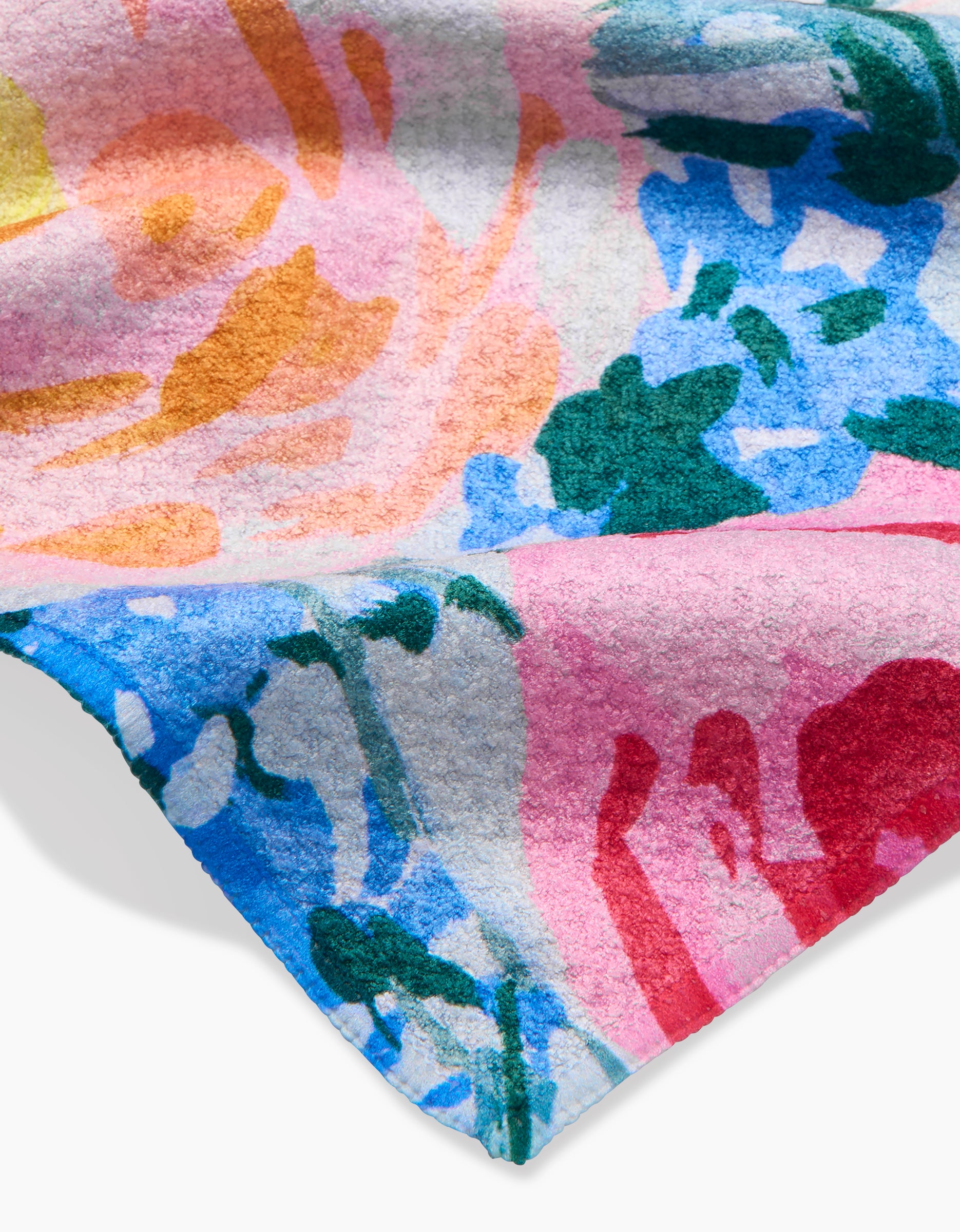 A close-up of the Suzzy dishcloth by Ania Zwara Art, made from soft Geoweave fabric. It features a vibrant abstract floral pattern in pink, blue, green, orange, and yellow with slightly folded edges that highlight its colorful style.