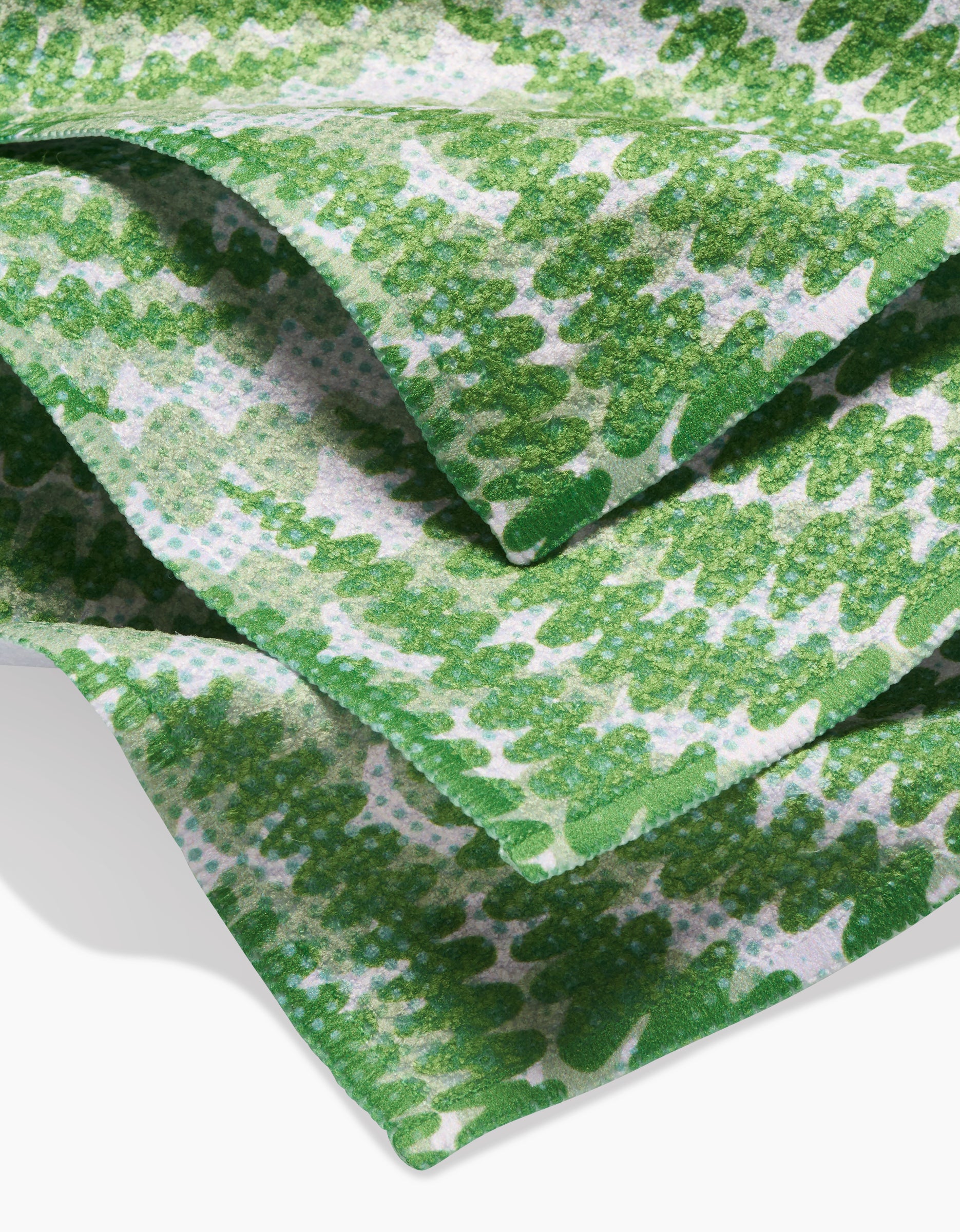 A close-up of GEOMETRY’s Swaying Leaf dishcloth shows overlapping folds of green and white Geoweave fabric with a zigzag design. The soft, lightly textured material is made from recycled materials.