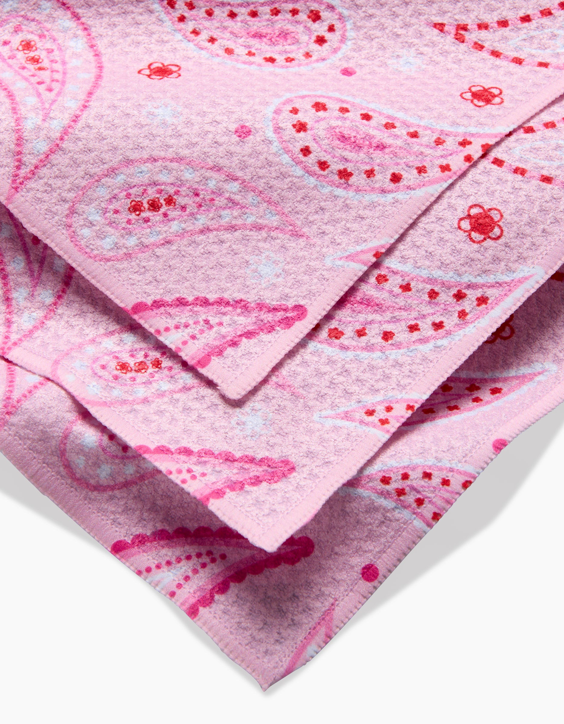 A close-up of the GEOMETRY Sweet Paisley dishcloth shows its folded, textured pink Geoweave fabric with a paisley and floral pattern in red, pink, and white.