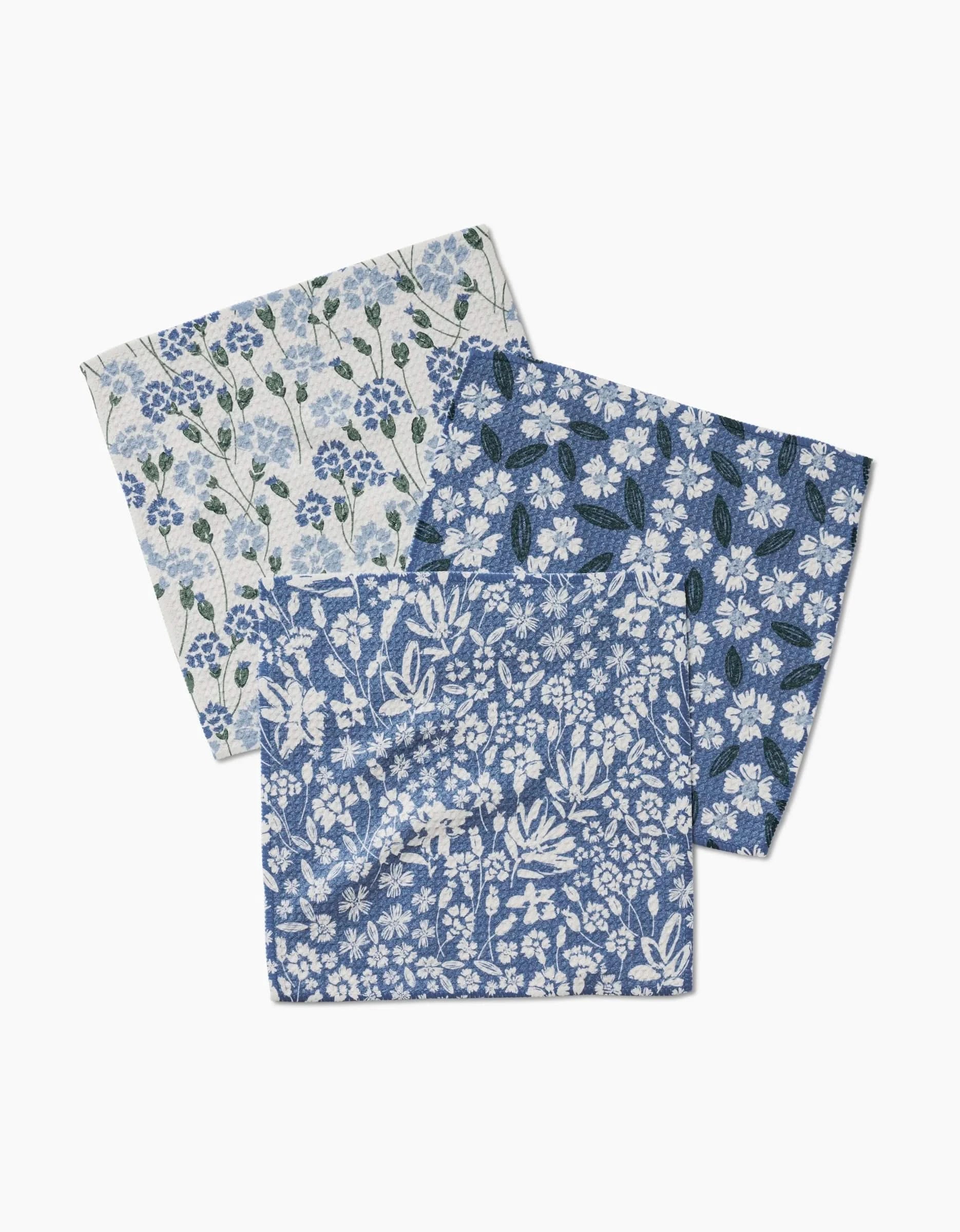 Three Sweetie Floral square napkins by Hufton Studio, each with unique blue and white botanical patterns, are overlapped on a white background—crafted from eco-friendly fabric for a sustainable touch.