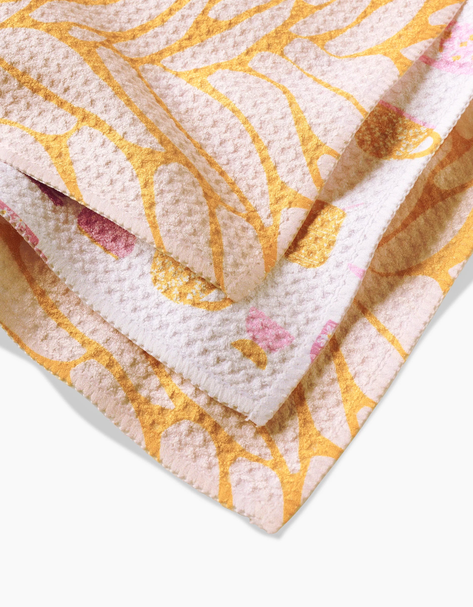 A close-up of GEOMETRY’s Tenderhearted towel, crafted from recycled materials, displays yellow and pink abstract lines and shapes on a textured white background.