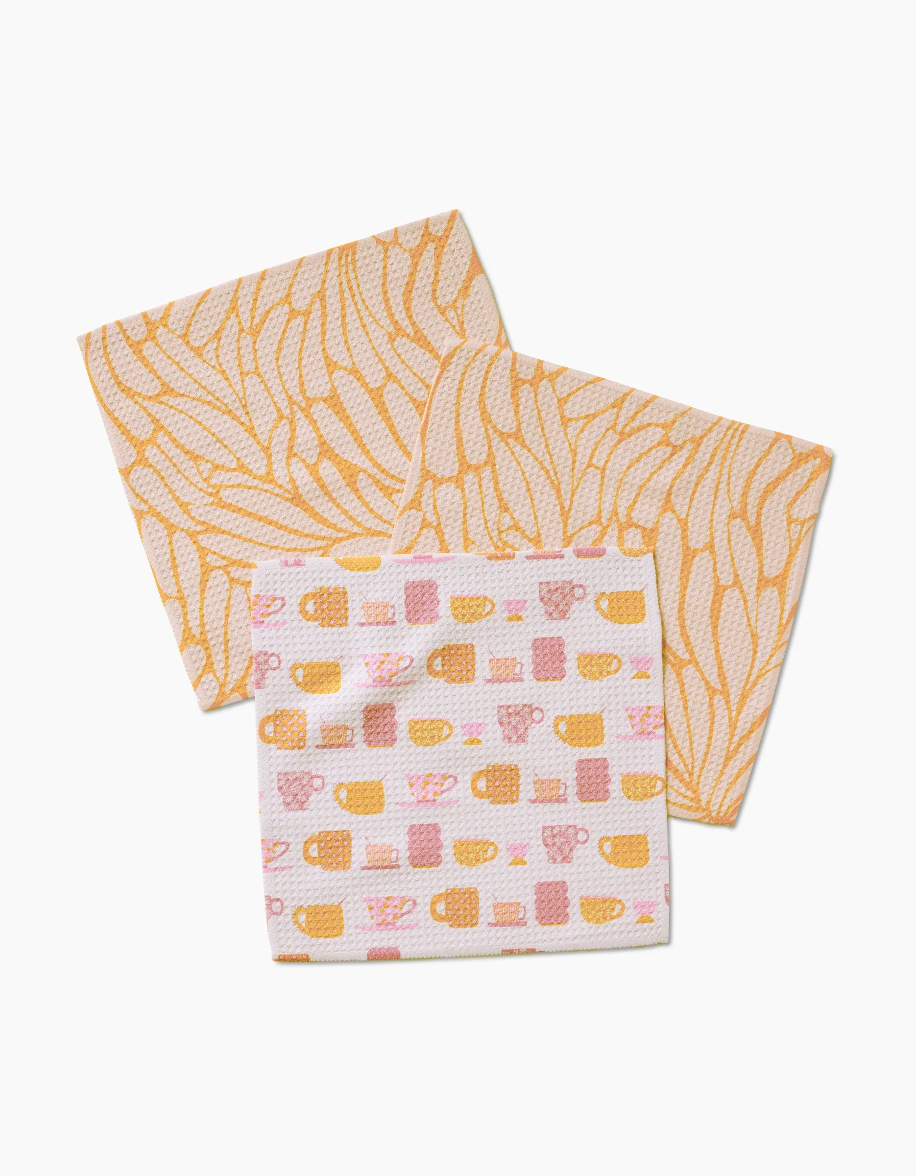 The Tenderhearted dishcloth set by GEOMETRY includes three Geoweave cloths: two with yellow abstract leaf designs and one featuring pink and yellow cups and mugs, all on a crisp white background.