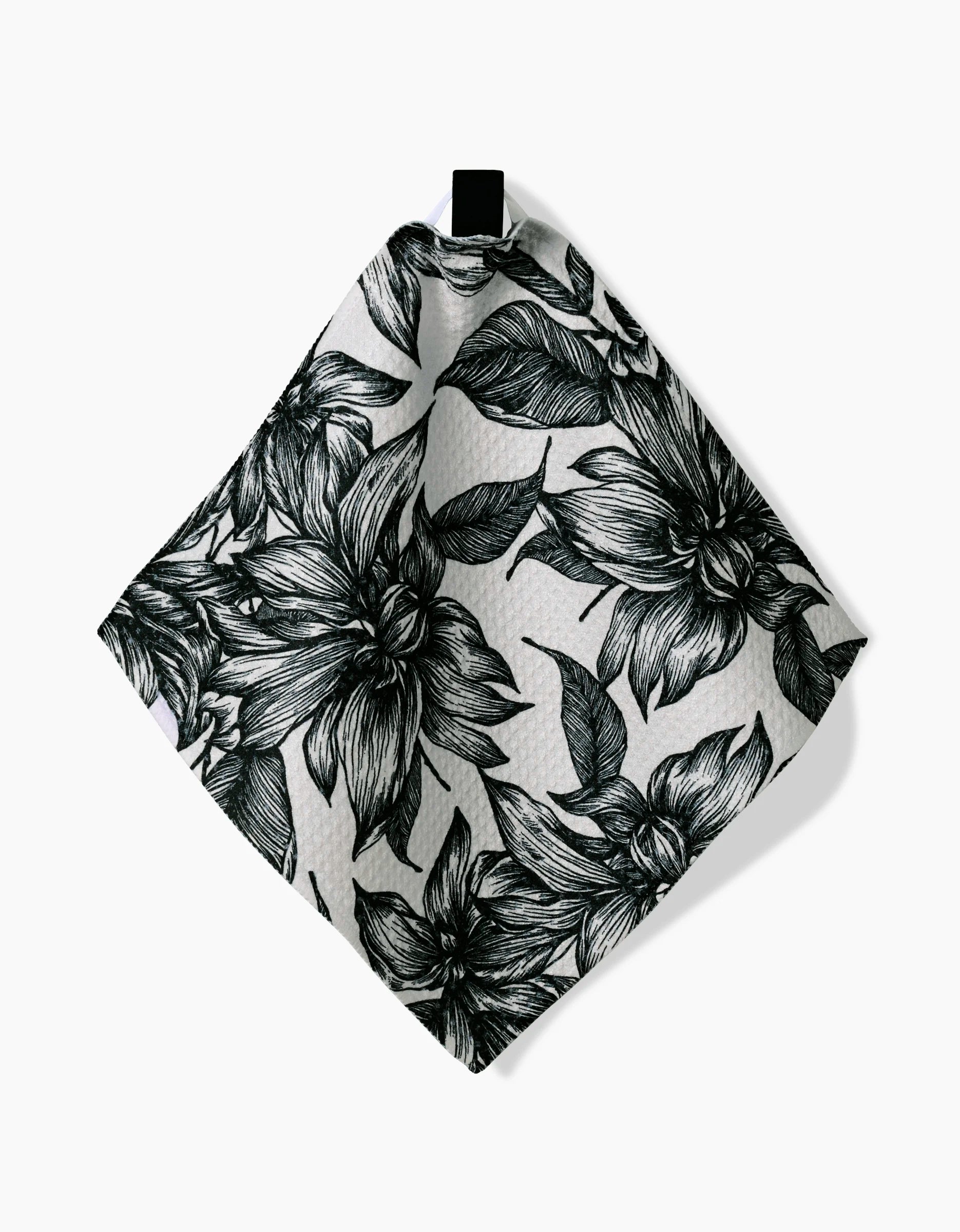The Best by GEOMETRY is a white recycled cloth napkin with a black floral pattern of large detailed flowers and leaves, shown hanging from a small black loop against a plain white background.