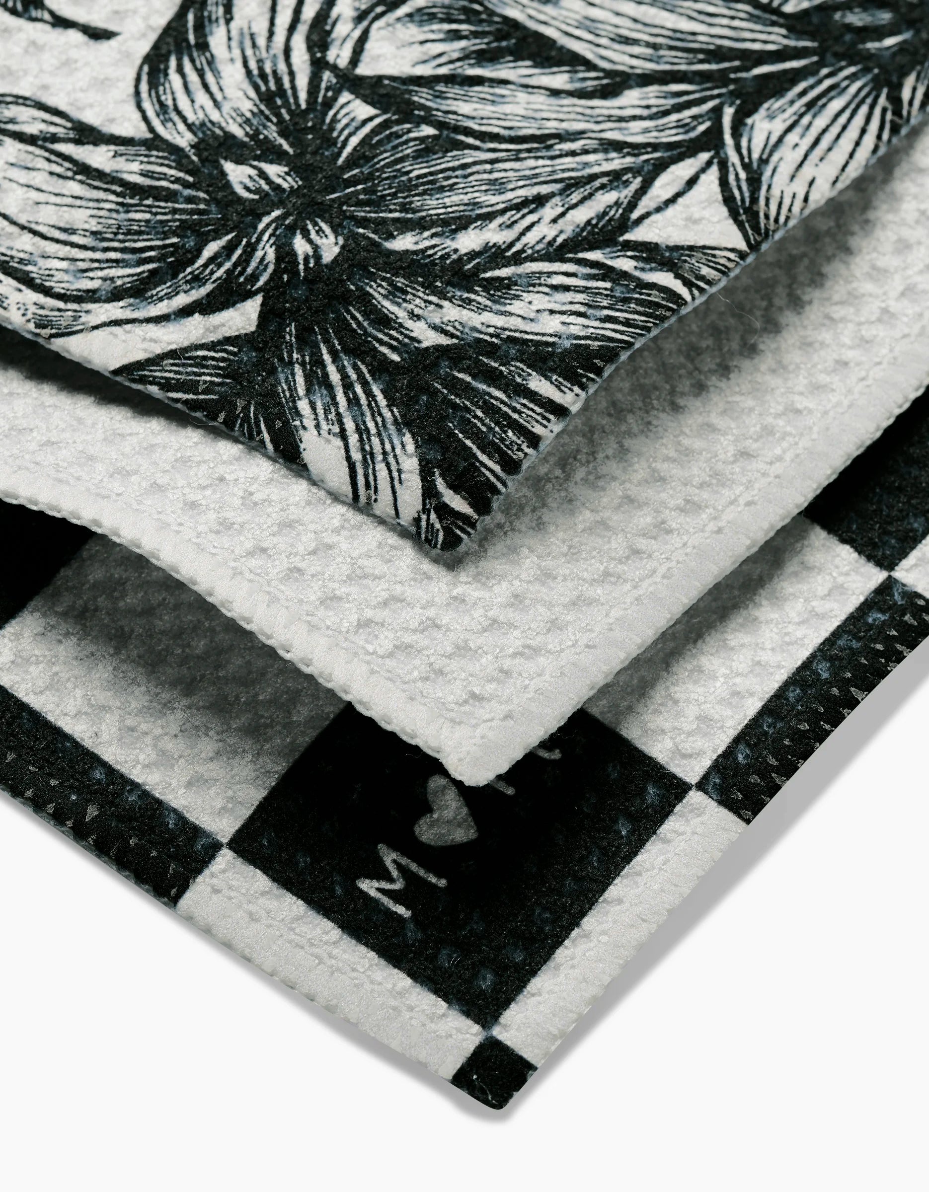 A close-up of two folded textiles: one with a black and white floral pattern, and another called The Best by GEOMETRY, featuring a checkered Geoweave fabric design and a visible woven texture.