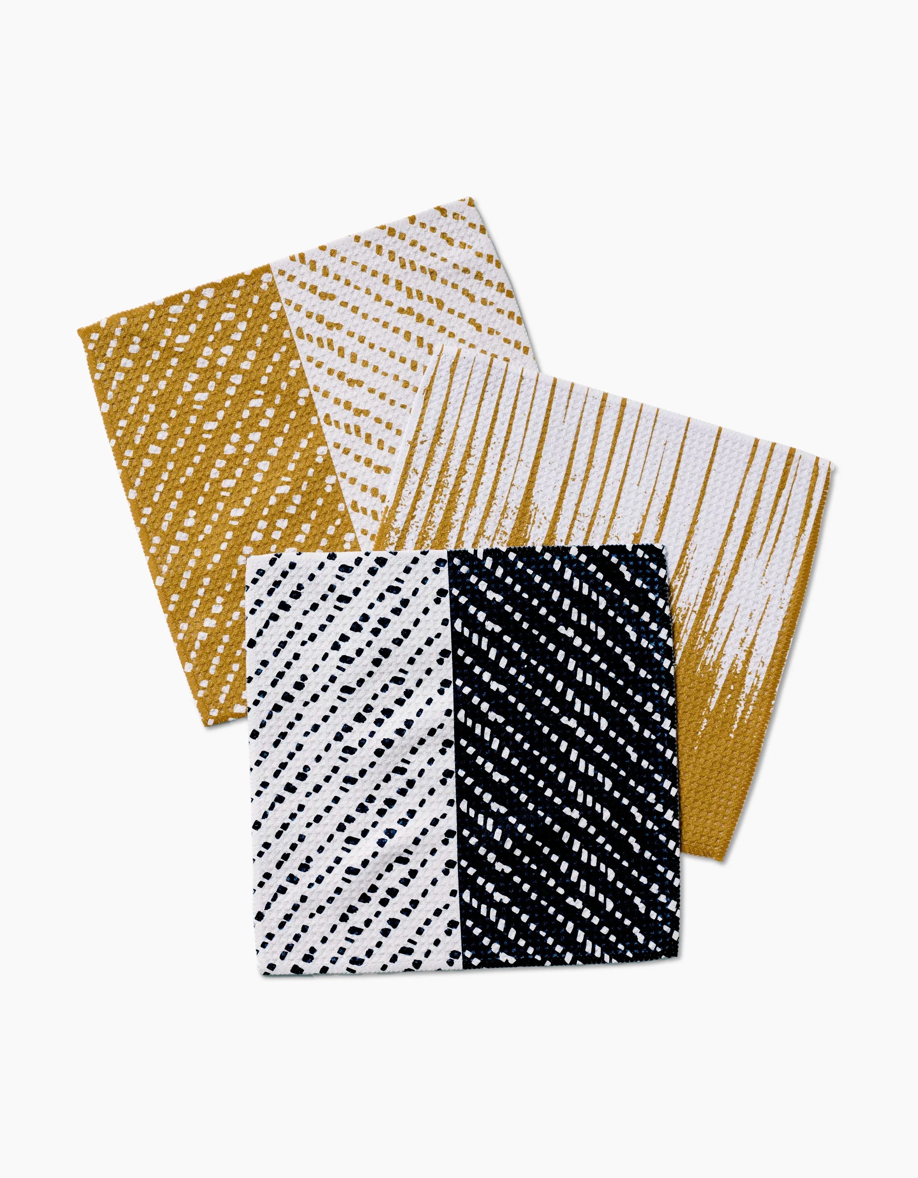 The GEOMETRY This And That set includes three rectangular dishcloths with diagonal dotted patterns in gold and white, white and gold, and half black with white dots/half white with black dots, crafted from innovative Geoweave fabric for superior cleaning.