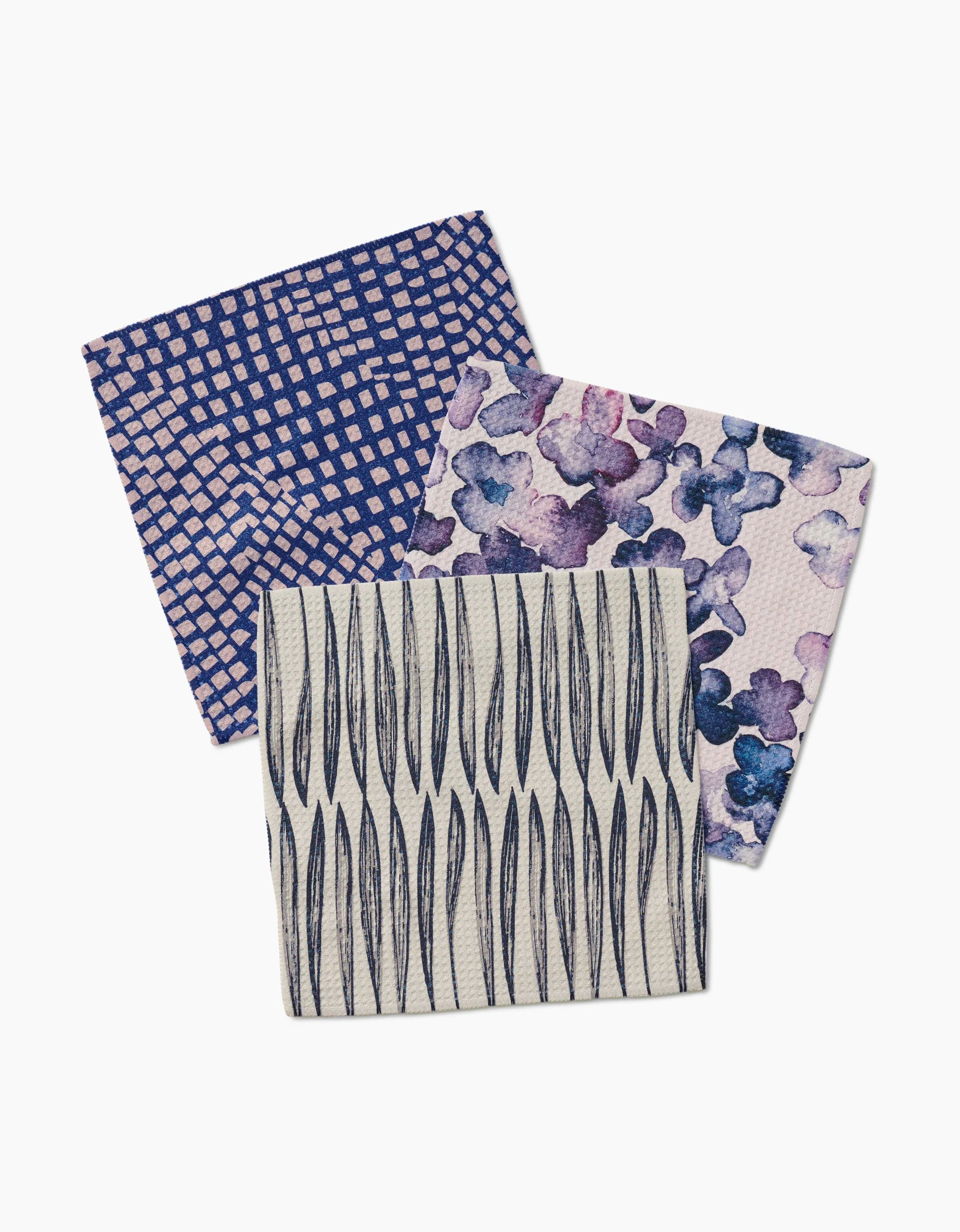 Three GEOMETRY dishcloths are shown: Tiny Petals with purple and blue floral patterns, a blue and tan checkered design, and a cream cloth with vertical black lines—all made from absorbent Geoweave fabric.