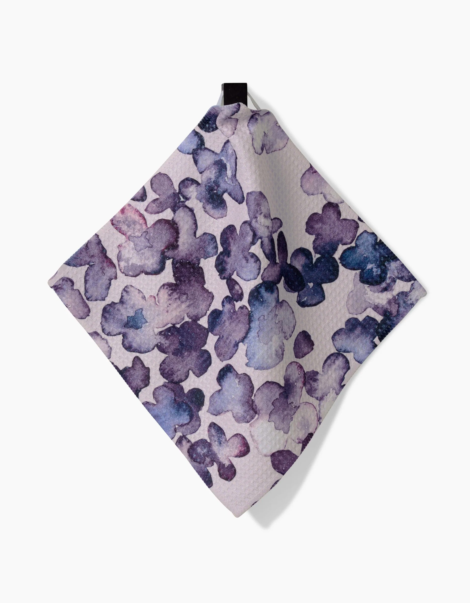 Tiny Petals by GEOMETRY: a square dishcloth featuring a watercolor-style purple and blue floral pattern, crafted from Geoweave fabric and shown hanging from a black loop against a white background.