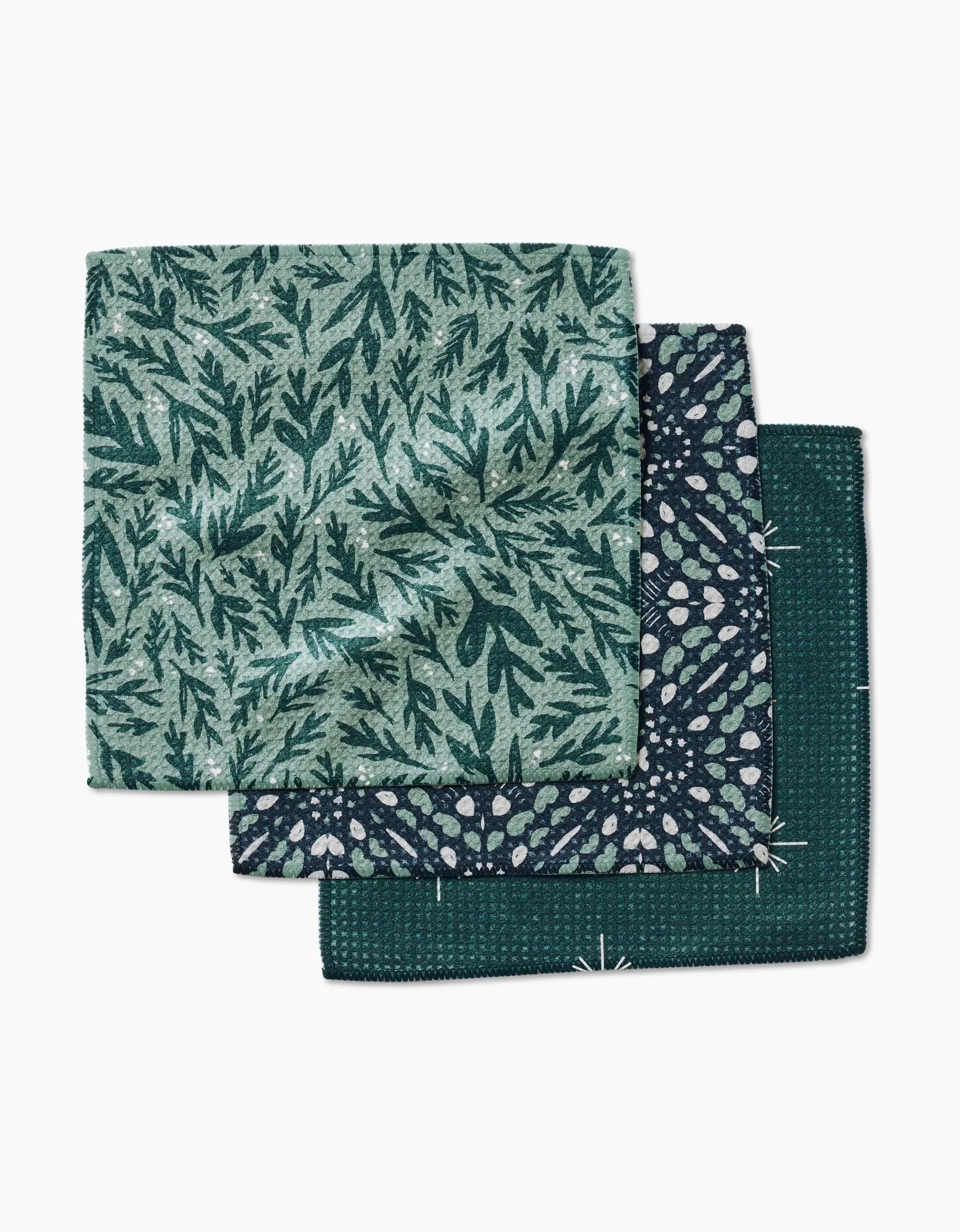 Three folded Twig + Spark Trail Dusting dishcloths in green and blue, each with a unique botanical or geometric pattern, are stacked—crafted from Geoweave fabric for extra softness and durability.