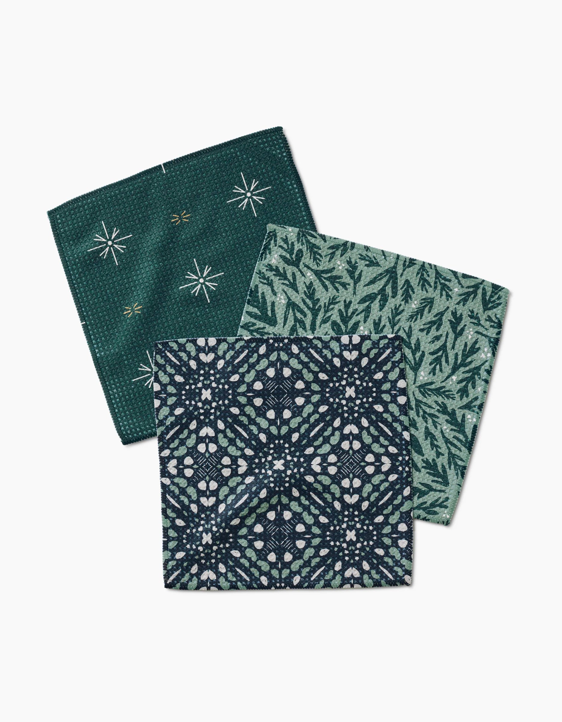 Three square napkins from Twig + Spark’s Trail Dusting set, made with recycled materials, showcase green and blue designs—stars and bees, leafy branches, and floral geometrics—all displayed on a white background.