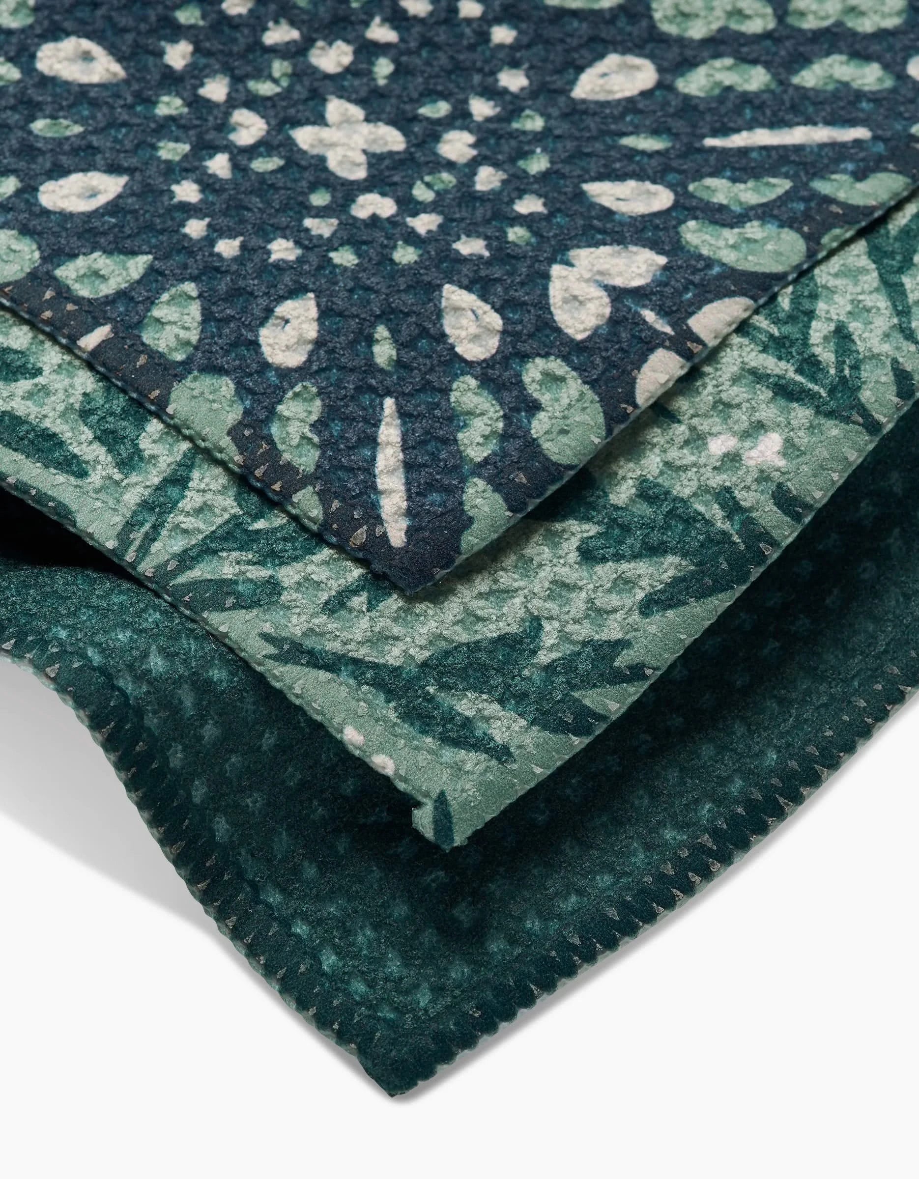 A close-up of three stacked Twig + Spark Trail Dusting dishcloths made from recycled Geoweave fabric, featuring soft, textured green and blue patterns like mandalas, leaves, and dots.