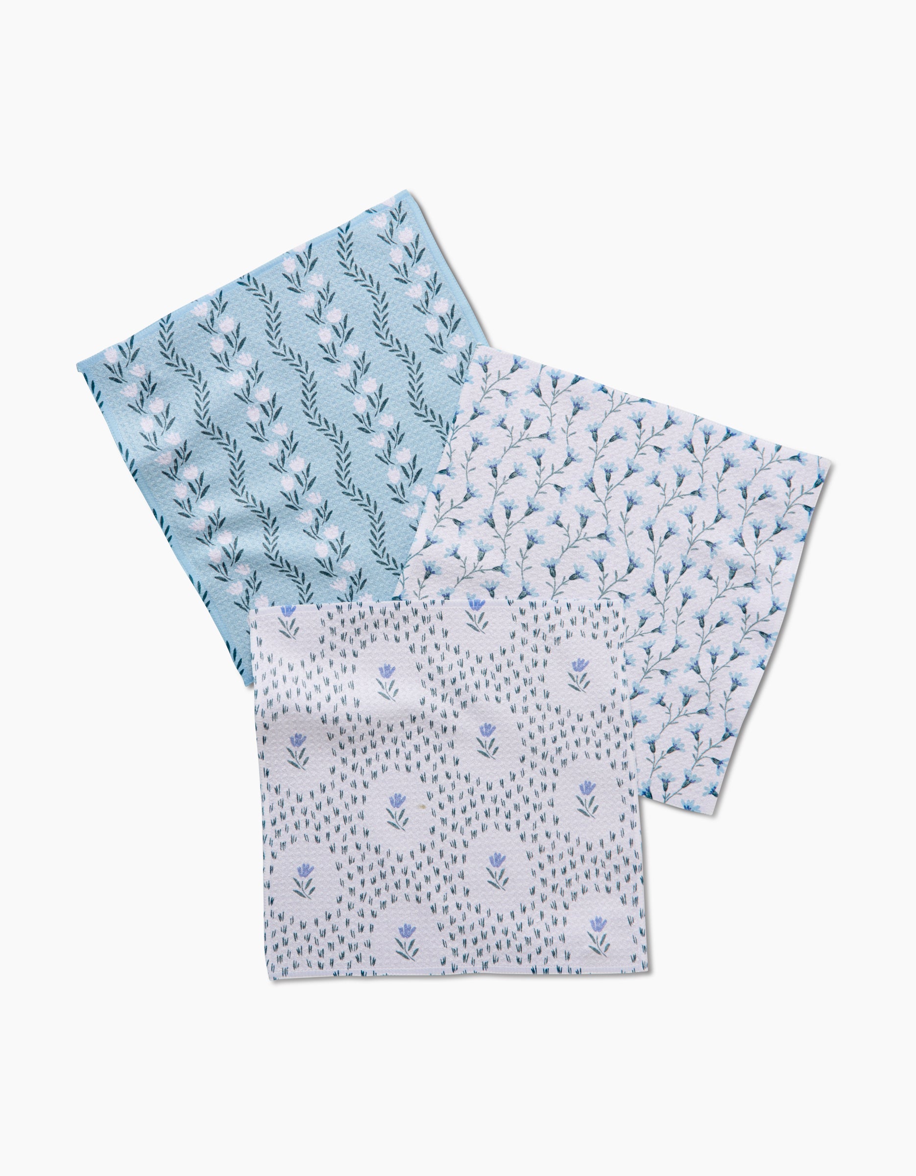 Three overlapping Trailing Farmhouse Florals dishcloths by Teri the Butter, each with a unique blue and white floral pattern, are crafted from durable Geoweave fabric and displayed on a white background.