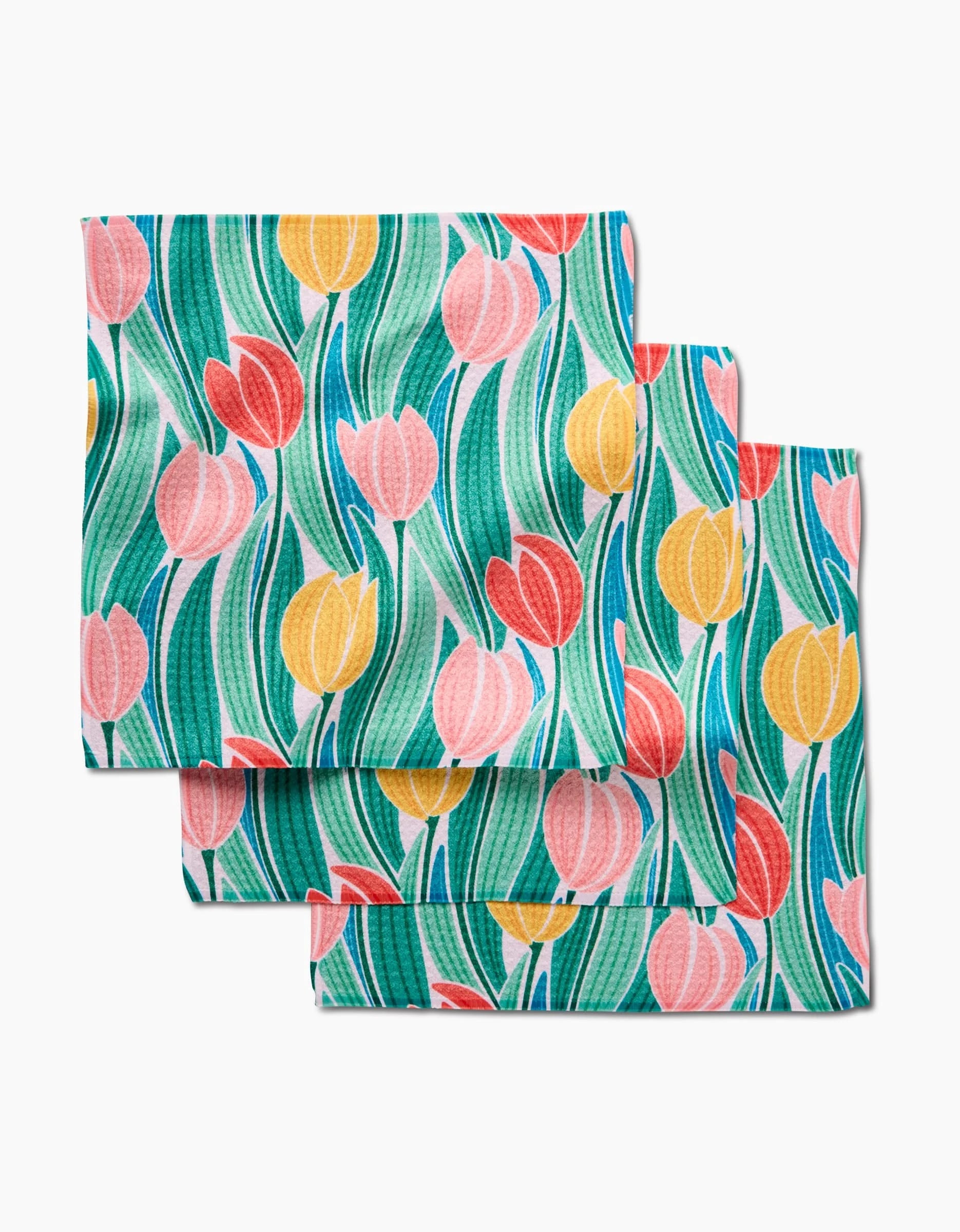 Three Tranquil Tulips cloth napkins by Sarah Daugherty, made from recycled materials, feature a vibrant tulip design in pink, yellow, and red with green leaves on a light background. The napkins are stacked in an overlapping arrangement.