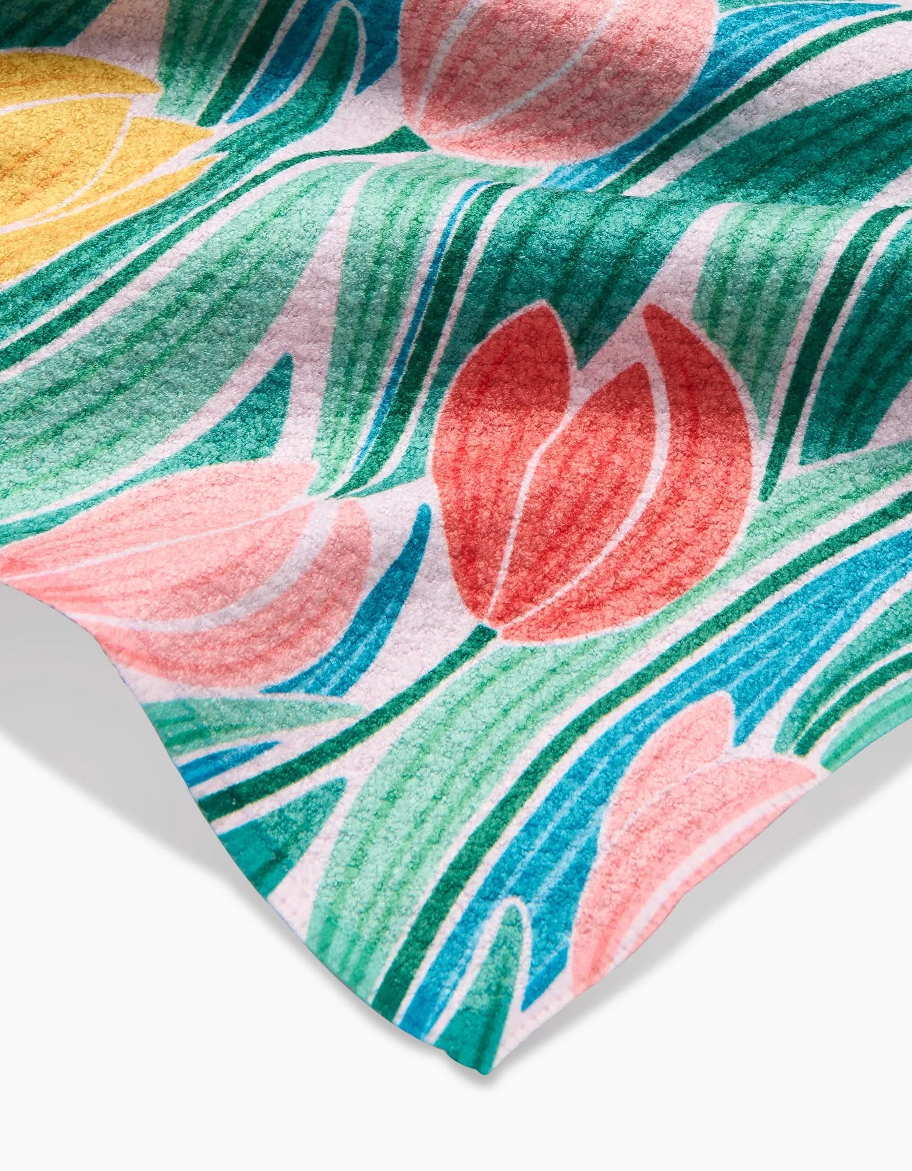 A close-up of the Tranquil Tulips dishcloth by Sarah Daugherty, featuring Geoweave fabric with a vibrant tulip pattern—pink, red, and yellow flowers with green leaves on a light background. The fabric’s edge appears in the lower corner.