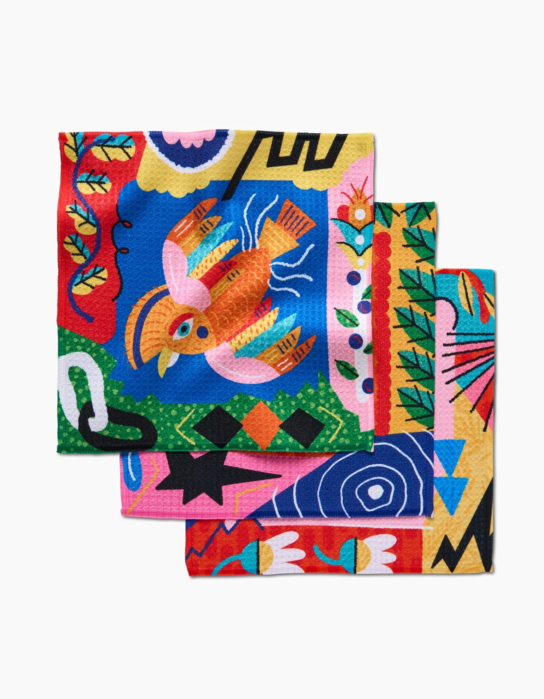 Three colorful Geoweave fabric napkins from Camila Leão’s Tropical Birds collection, neatly stacked and featuring bold, abstract designs in vibrant reds, blues, yellows, greens, and pinks.