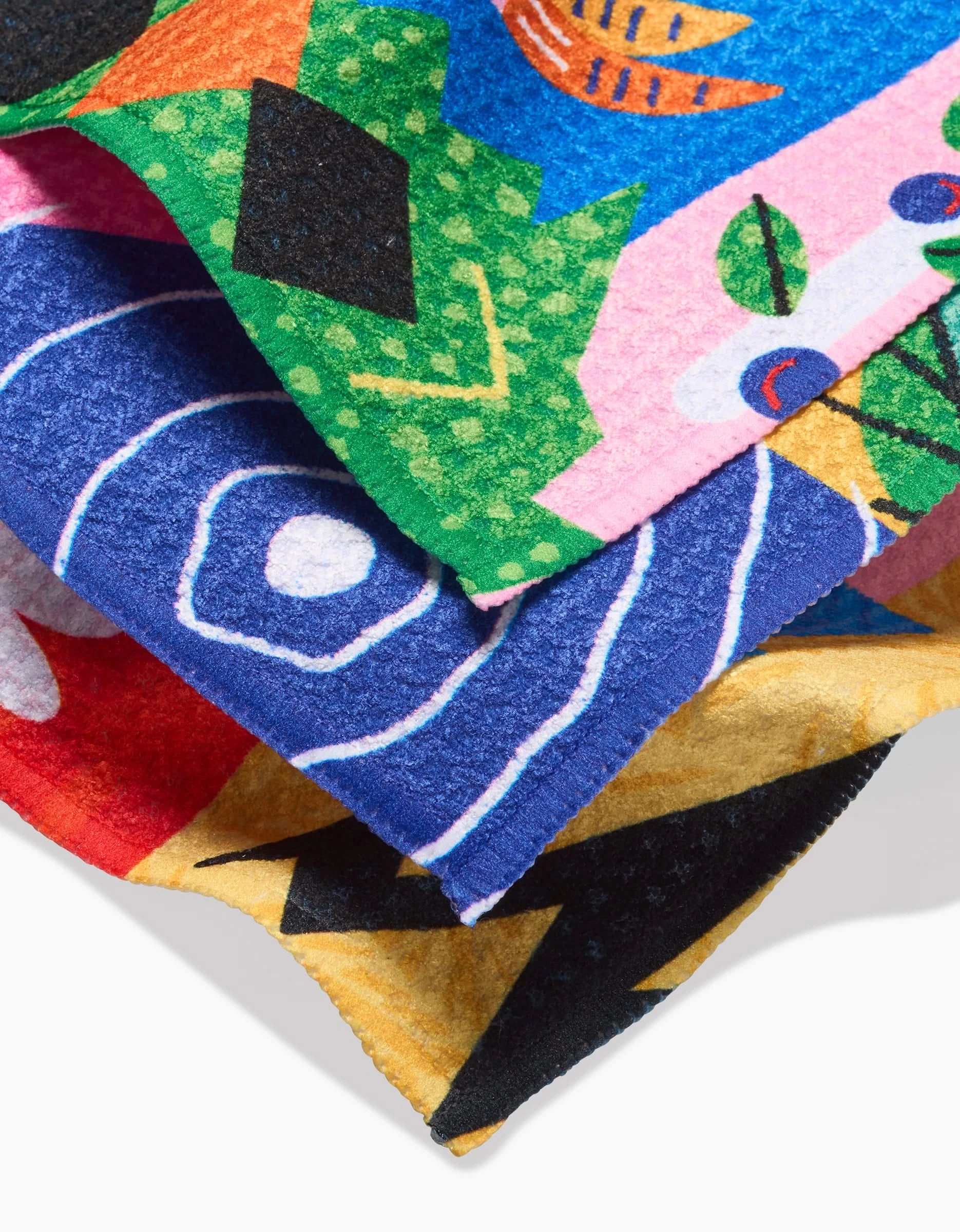 A close-up of three overlapping Camila Leão Tropical Birds Geoweave fabric pieces, featuring bold abstract patterns in green, pink, blue, red, yellow, black, and white with geometric and organic shapes.