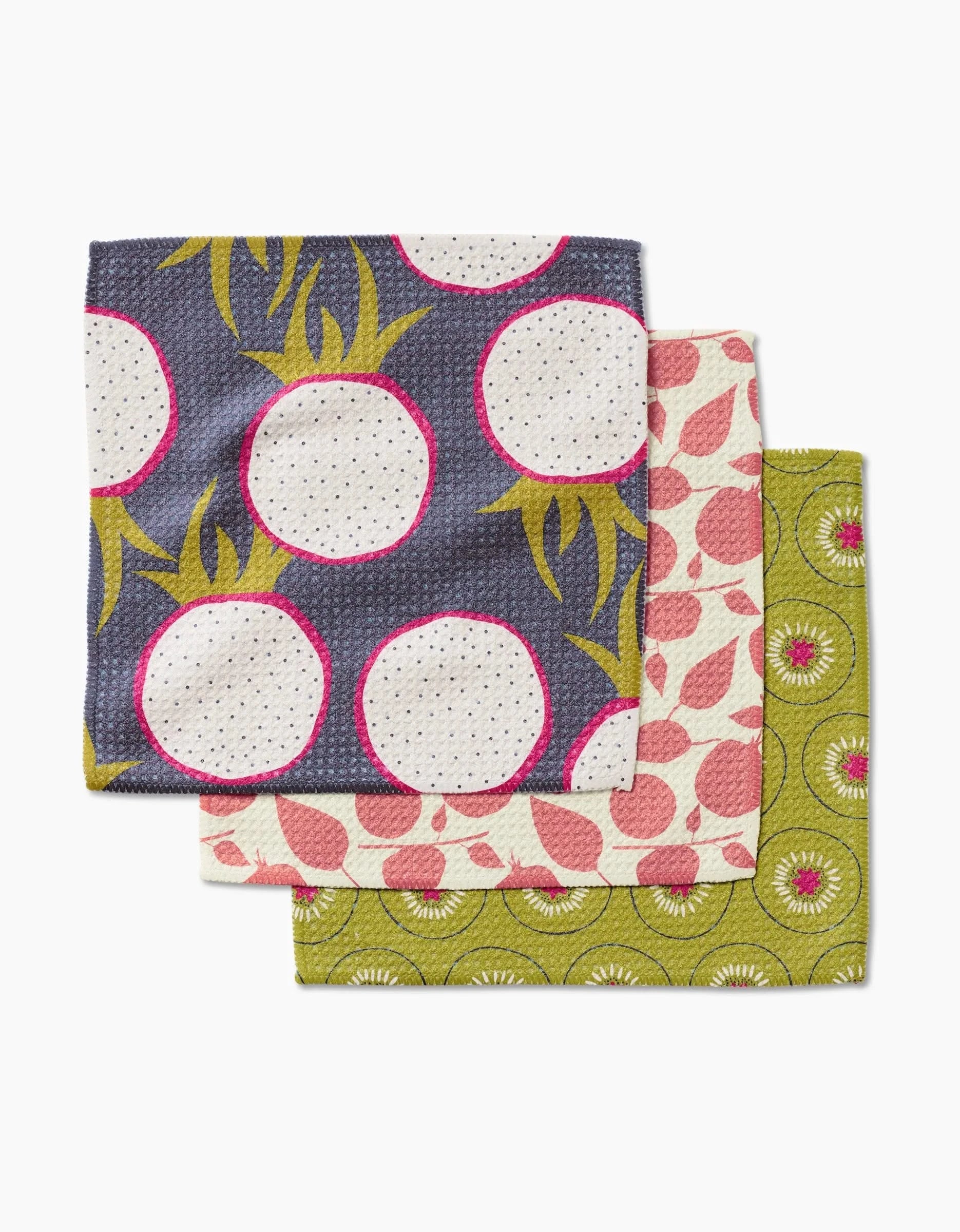 The Lizzie Clark Tropical Fruit Dishcloth Set includes three super-absorbent Geoweave towels in vibrant patterns: white radishes on dark blue, pink leaves on light pink, and green kiwi slices.
