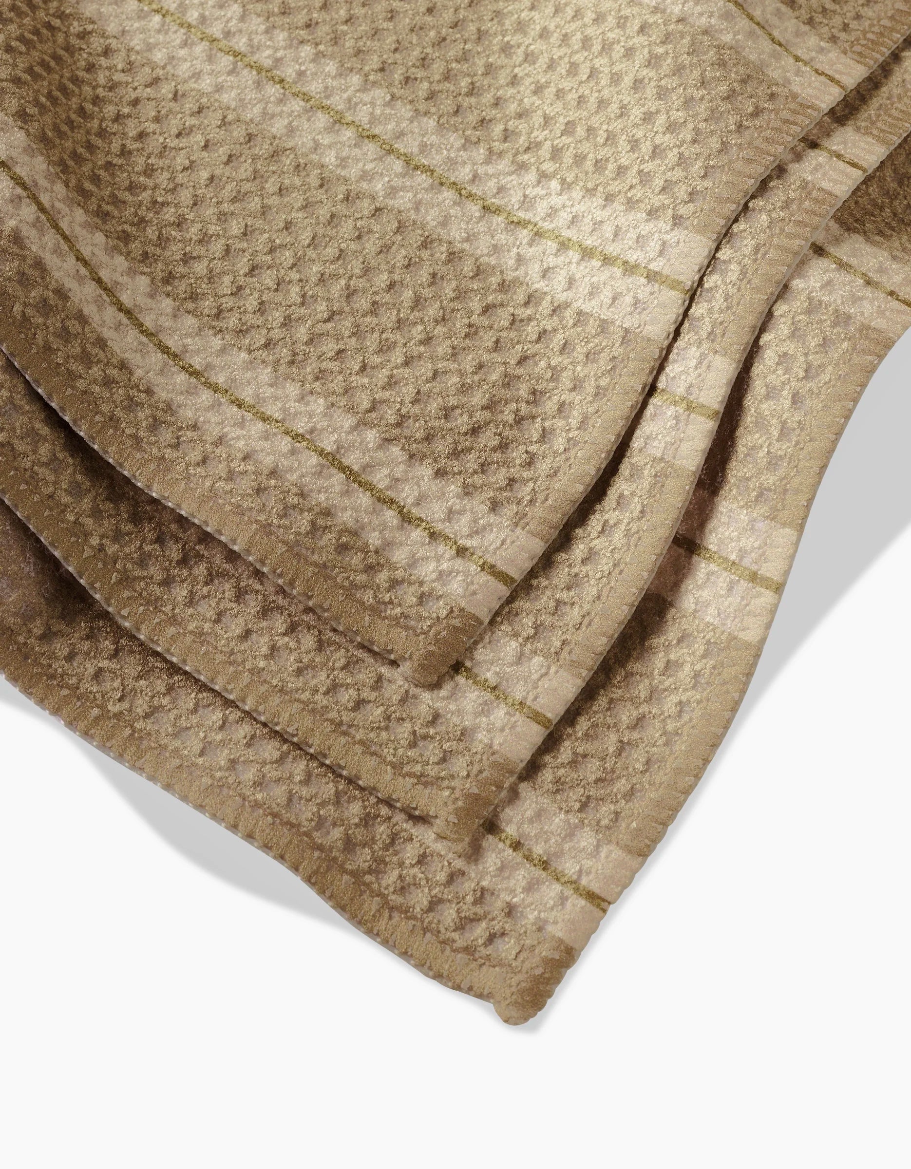 A close-up of folded GEOMETRY’s Vanilla Chai Geoweave fabric in light brown, showcasing a subtle plaid pattern with intersecting lines and a waffle-like texture.