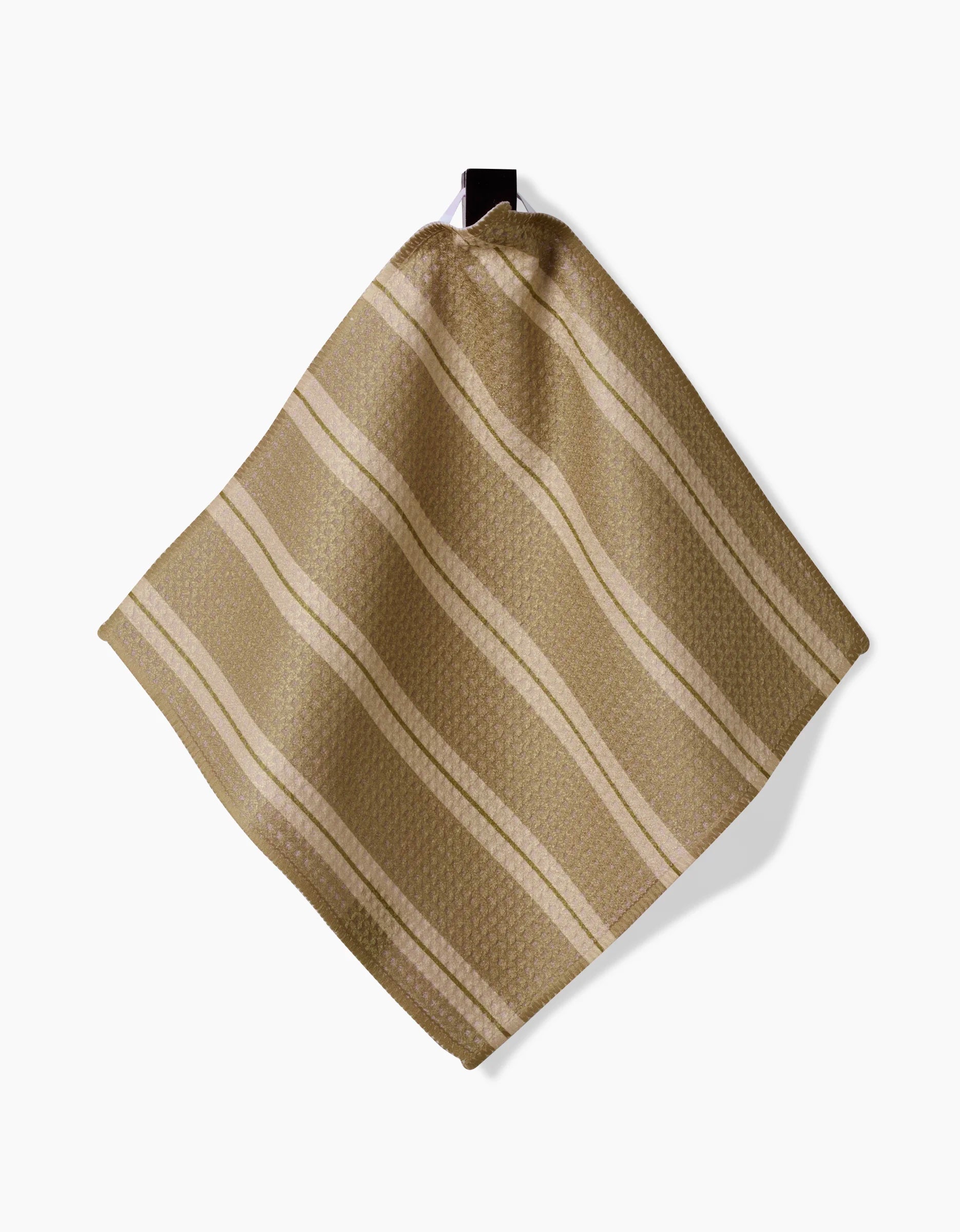 The GEOMETRY Vanilla Chai dishcloth, featuring beige and light brown stripes in Geoweave fabric, hangs from a black hook against a white background.