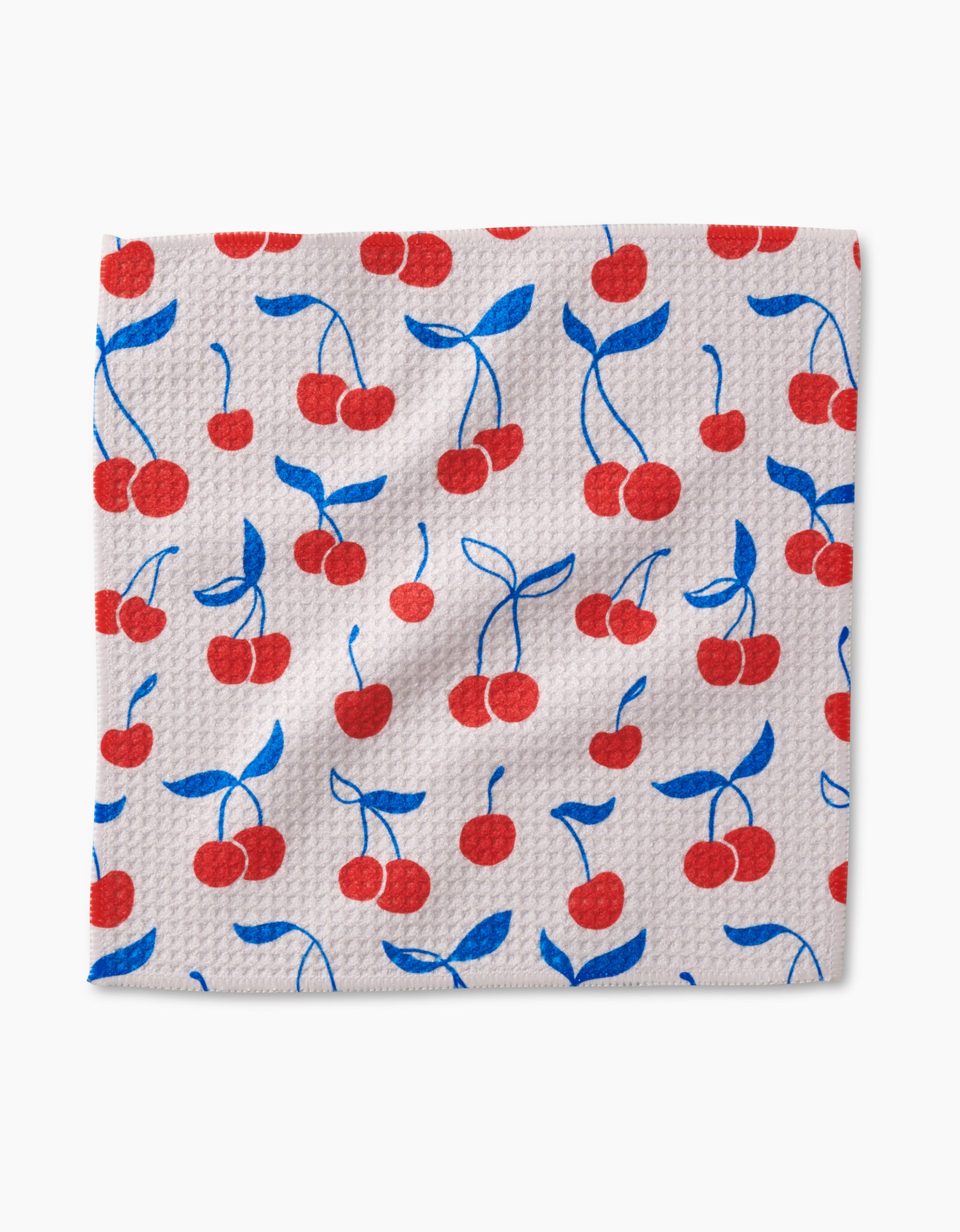 The Very Cherry dishcloth from Kayla Ann features a white textured Geoweave fabric with a playful red cherry pattern accented by blue stems and leaves—stylish, absorbent, and perfect for your kitchen.