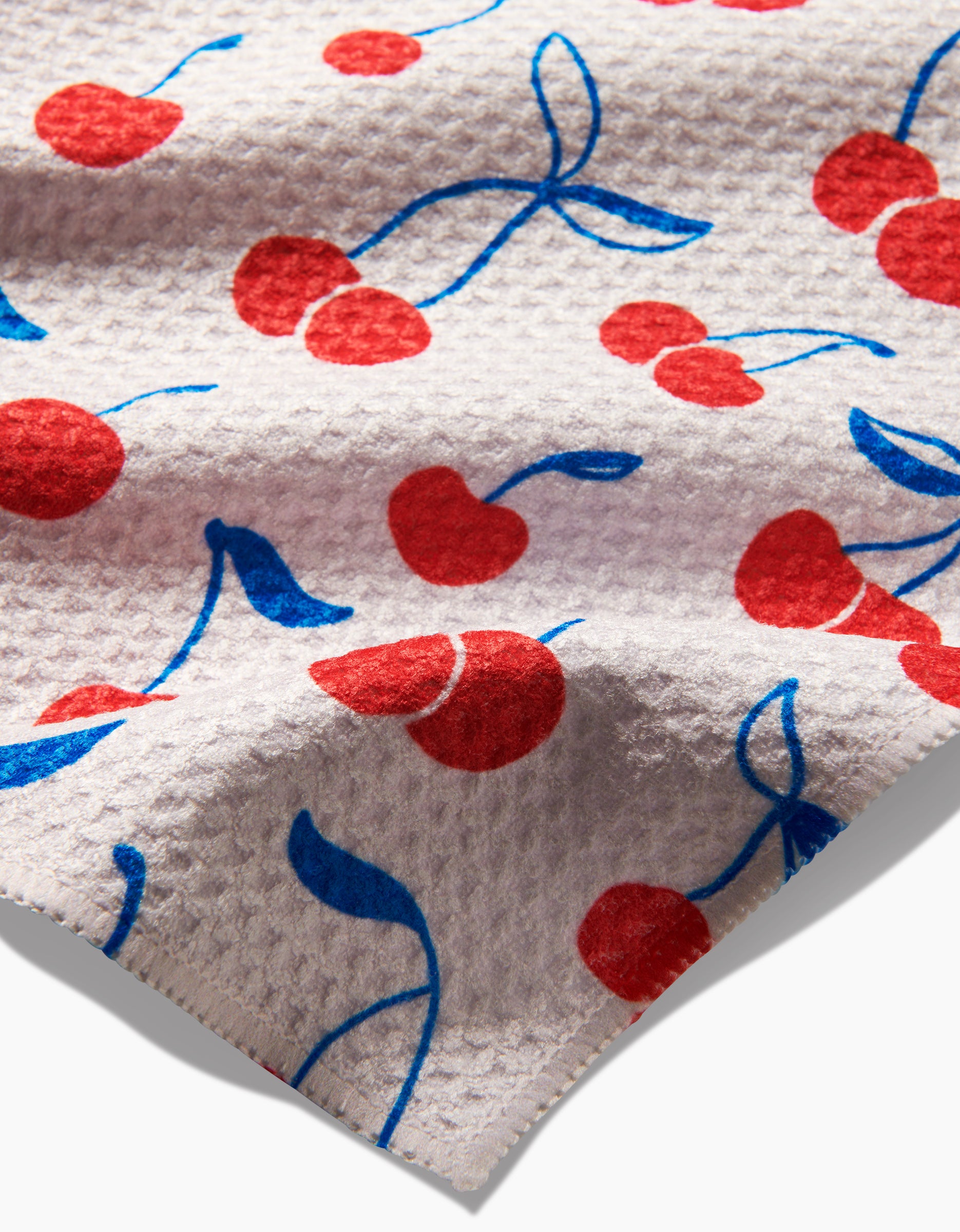 Kayla Anns Very Cherry dishcloth features textured white Geoweave fabric with a playful pattern of red cherries and blue stems, making it super-absorbent and perfect for kitchen use.