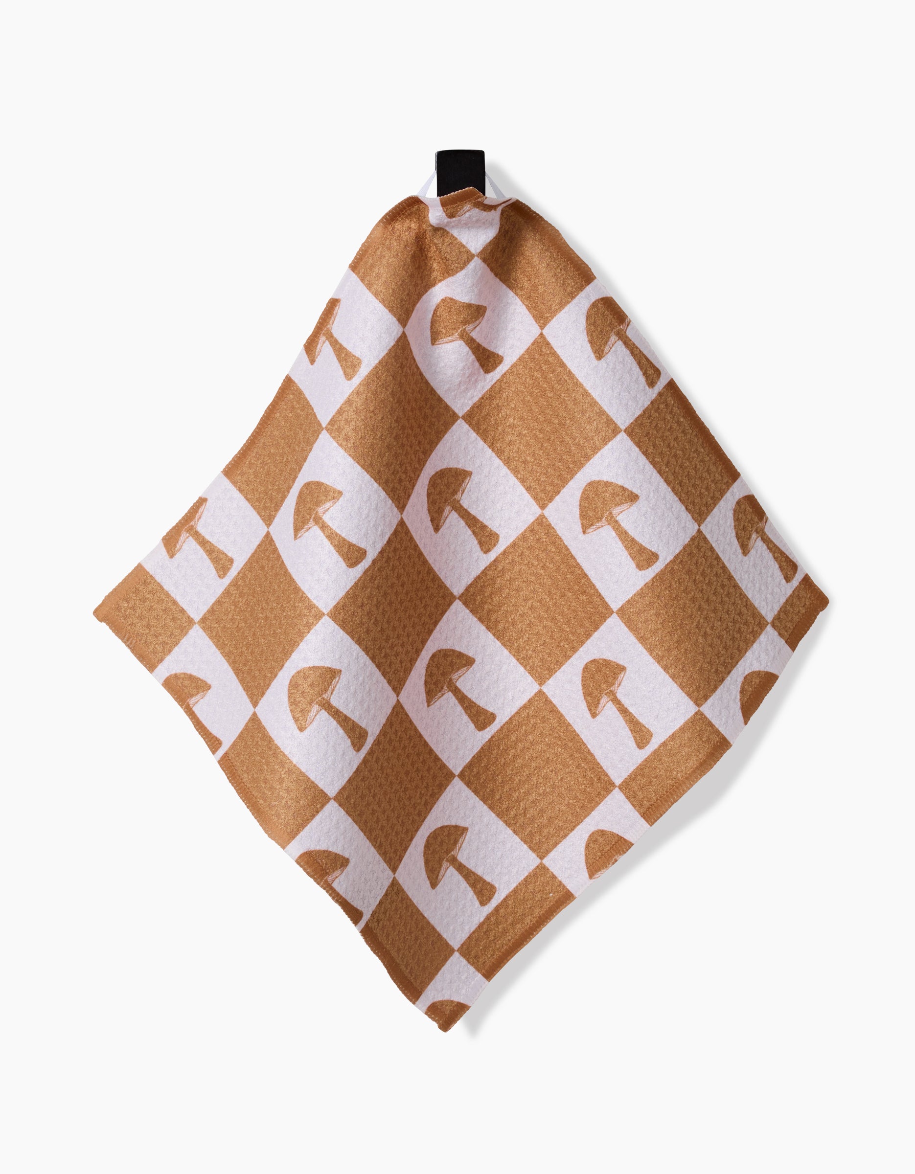 The Vines Acorns And Mushrooms dishcloth by Charlie Rowan Designs features Geoweave fabric with a tan and white checkered pattern, brown mushroom illustrations on the white squares, and hangs from a black loop.
