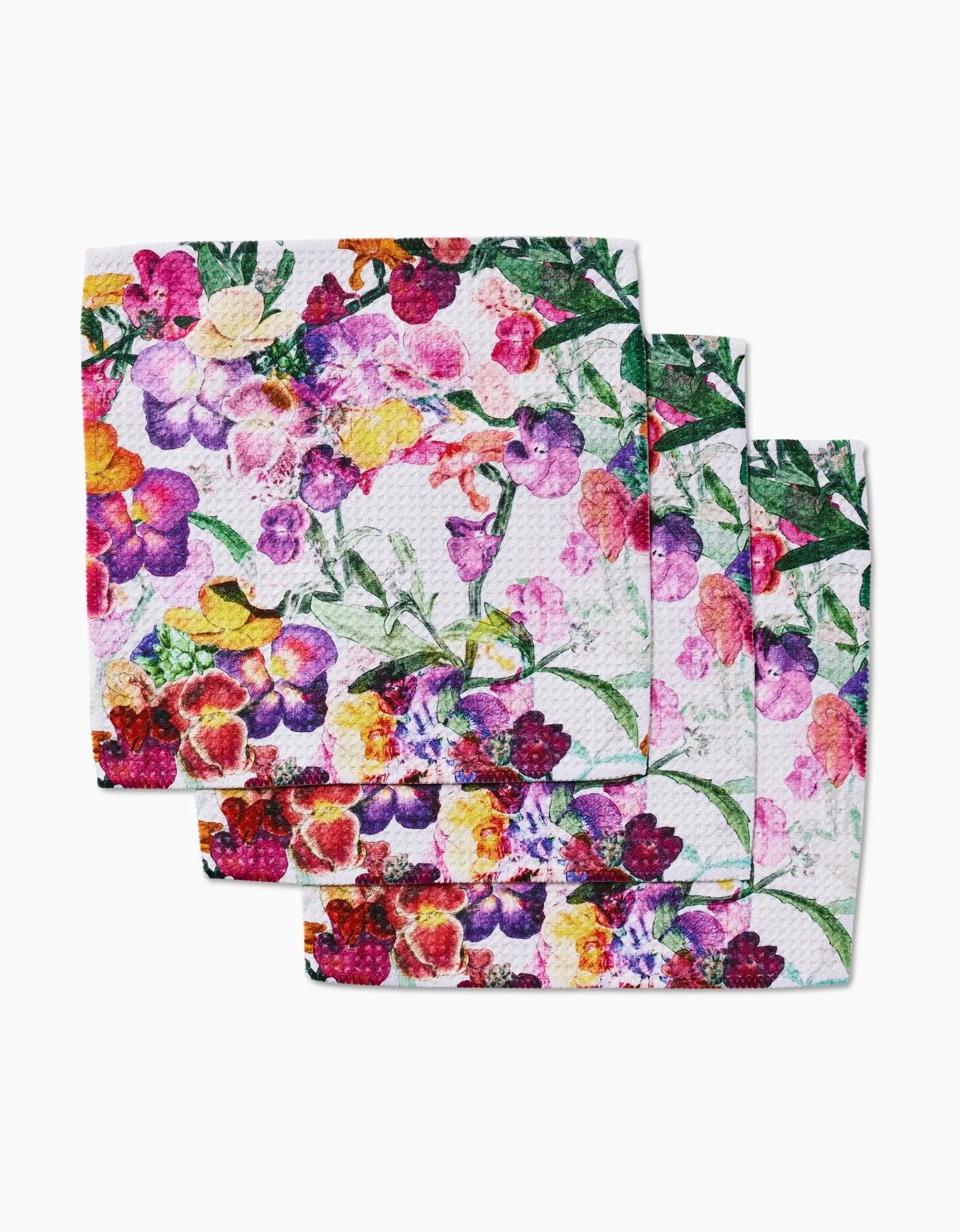 Four square Pascale Dilger Wallflower napkins, made from recycled materials, feature a colorful floral pattern in pink, purple, yellow, and green and are arranged in a slightly overlapping stack on a white background.