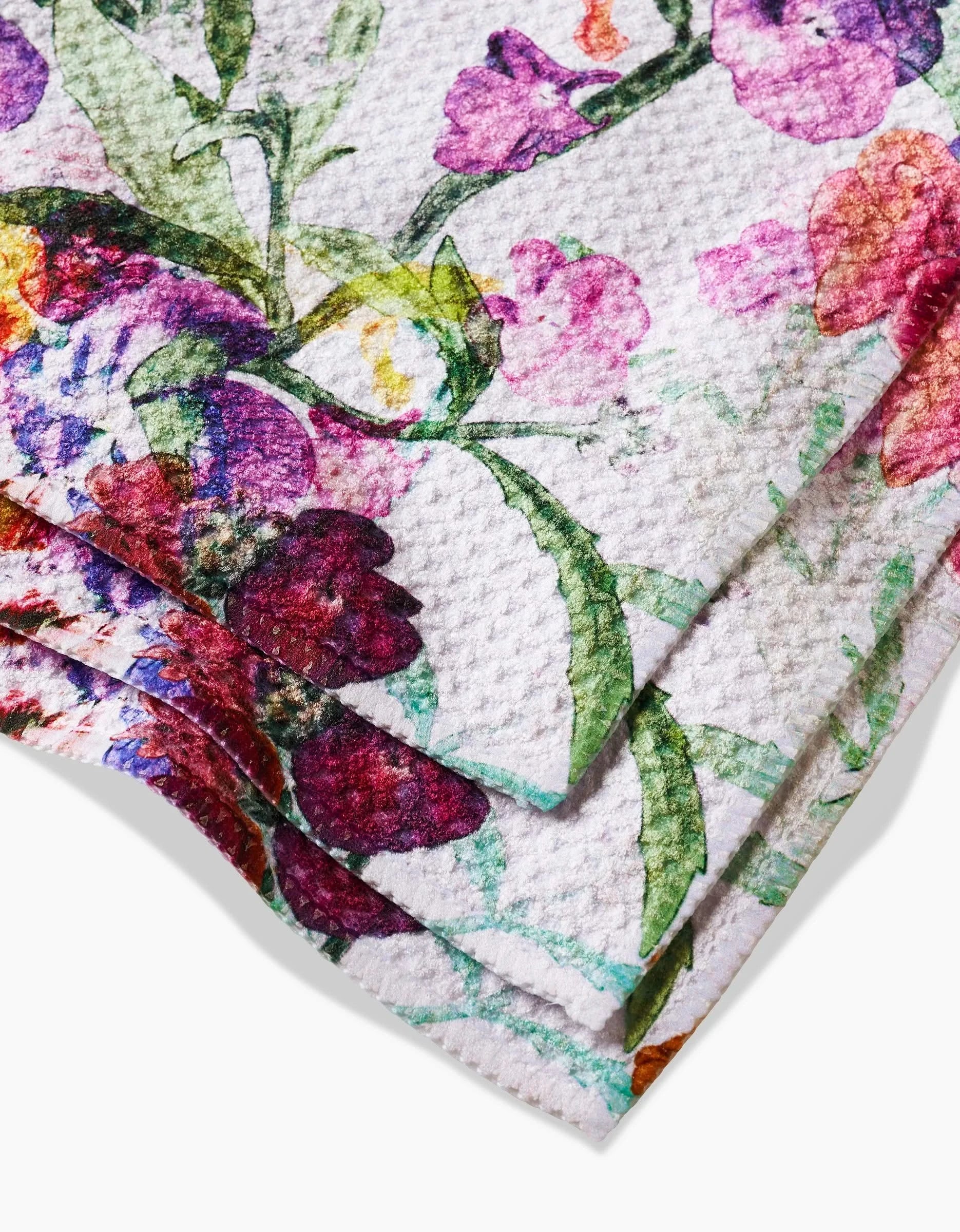 A close-up of three folded Pascale Dilger Wallflower paper towels, showing a colorful floral print with pink, purple, red, and green flowers and leaves on textured white recycled material.