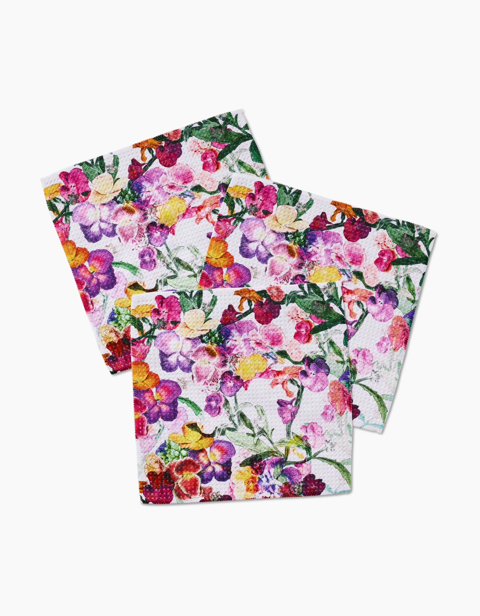 Three Wallflower napkins by Pascale Dilger, made from recycled materials, display overlapping pink, purple, yellow, and green floral prints on a white background.
