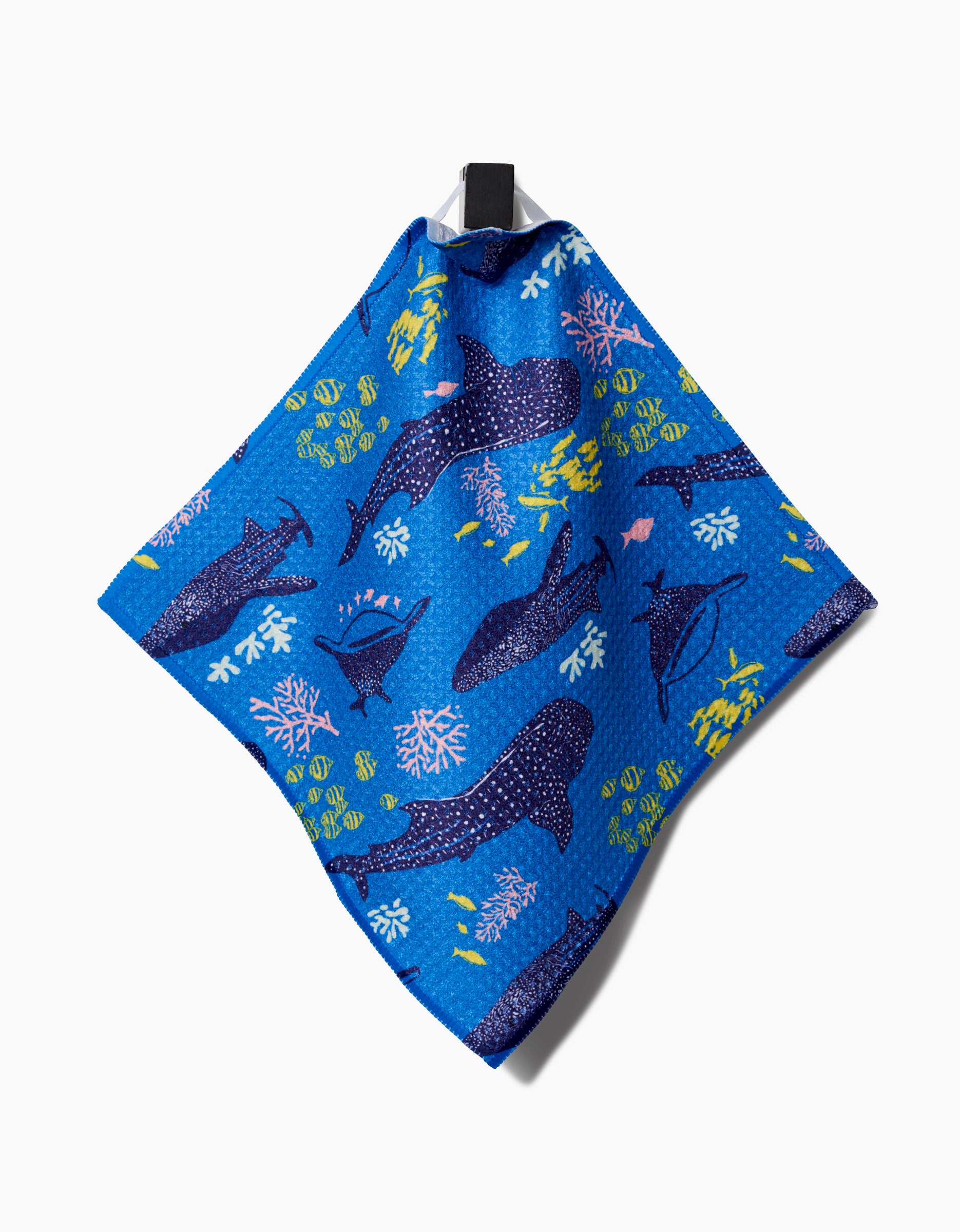 A blue Elisabeth Wing Whale Shark Geoweave dishcloth made from recycled materials, with whale, turtle, fish, and coral illustrations, hangs from a black loop against a white background.
