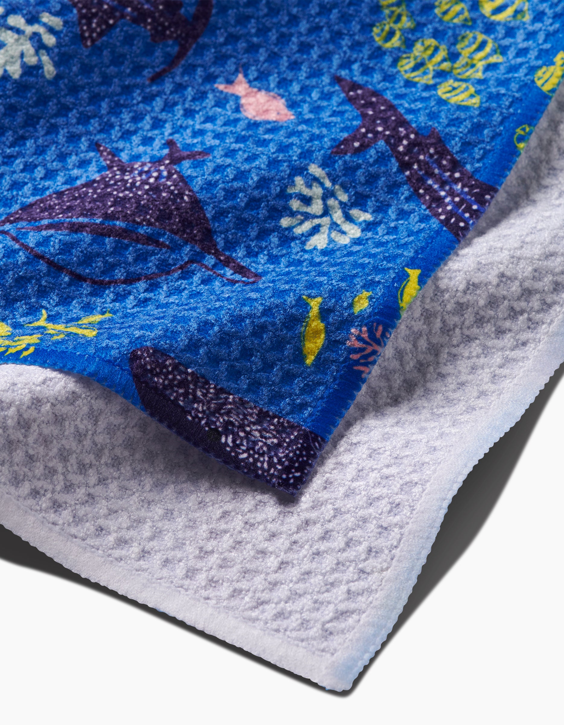 A close-up of the Elisabeth Wing Whale Shark Geoweave towel shows sea animals like whales, fish, and coral on blue, with a white textured underside. Made from recycled materials, this stylish dishcloth offers sustainability.