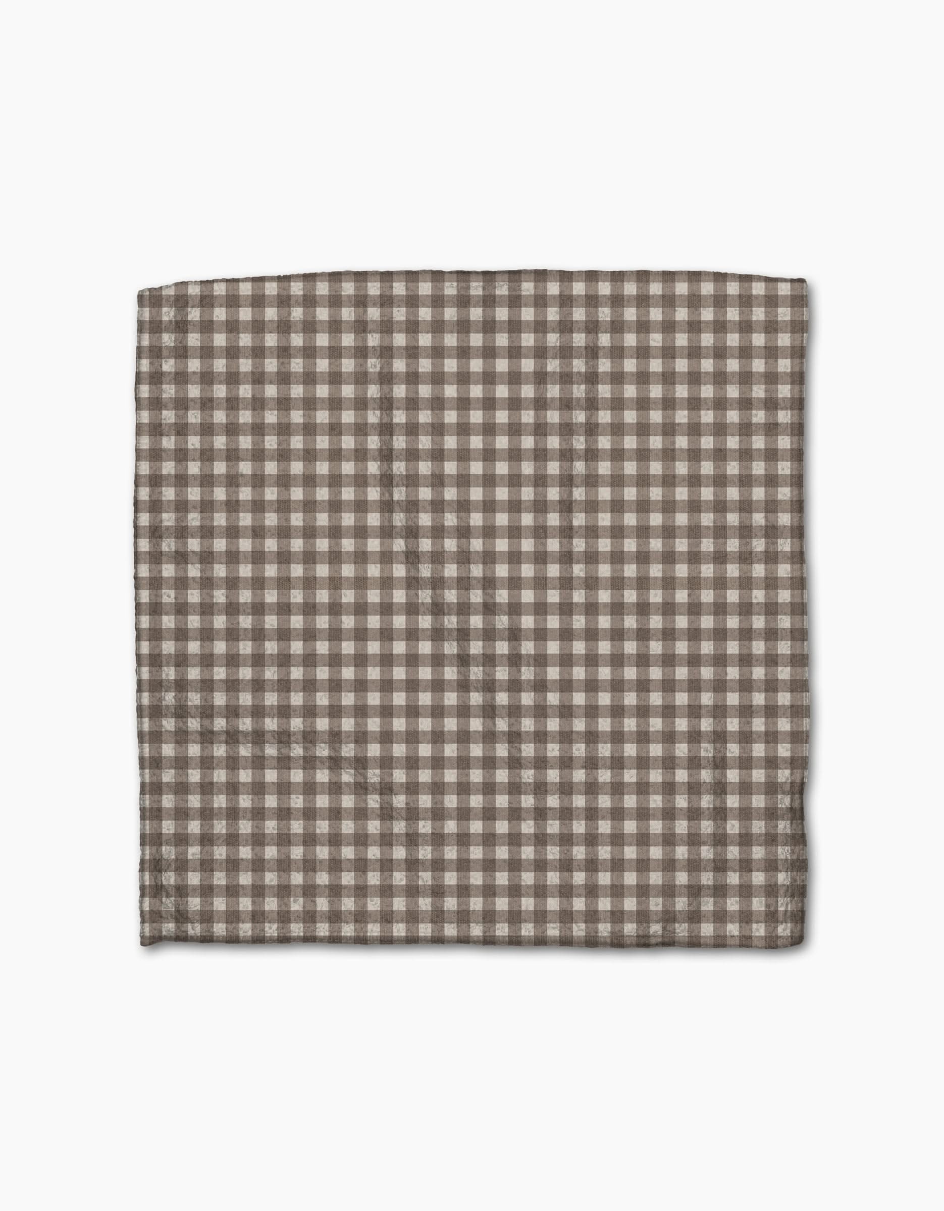 The Whidbey Check cloth napkin by Jenny Keller, in brown and white checkers and made from recycled materials, is neatly folded and displayed against a plain white background.