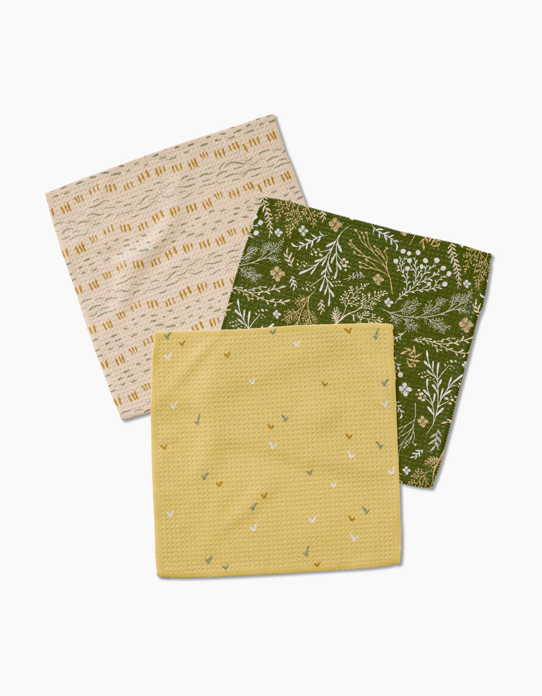 Three Danelys Sidron “Wildflowers” dishcloths, crafted from Geoweave fabric, feature tan with brown lines, green with white florals, and yellow with multicolored sprigs. They are arranged overlapping on a white background.