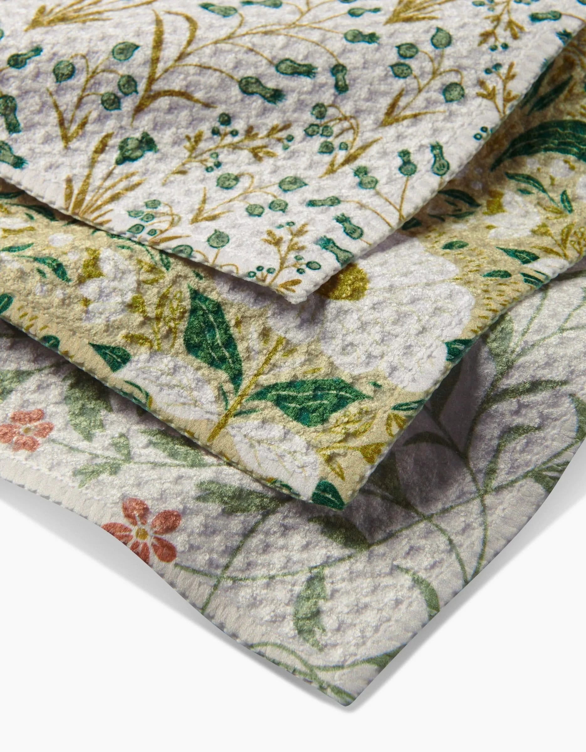 The Danelys Sidron Wildlight set includes three overlapping Geoweave dishcloths with unique floral patterns in green, gold, red, and blue on light backgrounds. Each is crafted from recycled materials and features leaves, flowers, and stems.
