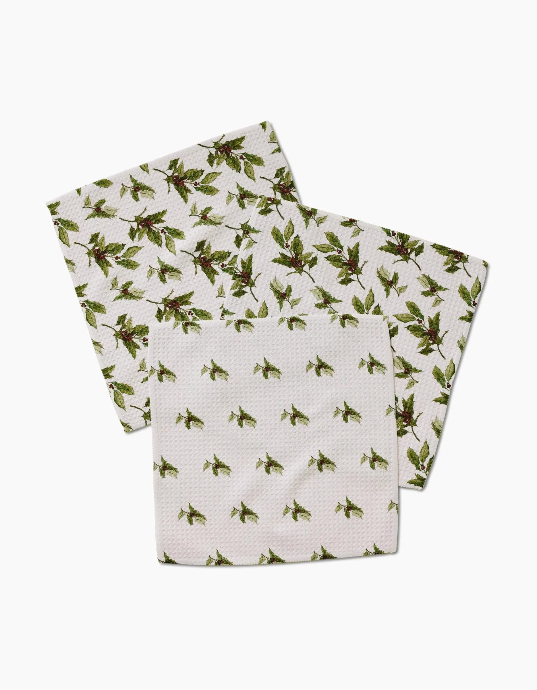 Three Winter Berry napkins by Aubrey Fairchild, made from Geoweave fabric in white with a green holly and red berry pattern—two in a dense design and one spaced out—are arranged on a white background.