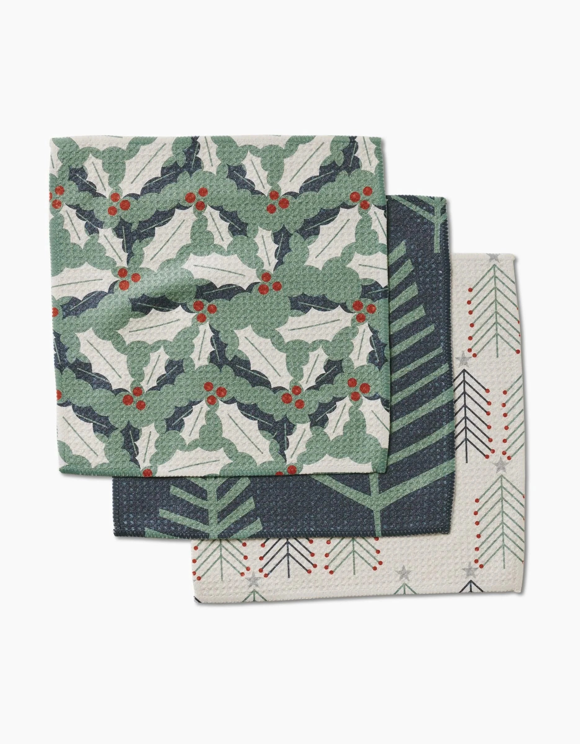 The Lizzie Clark Winter Wonderful set includes three holiday-themed Geoweave dishcloths: one with holly and berries, one dark with green tree branches, and one light featuring a line-drawn tree with red accents.