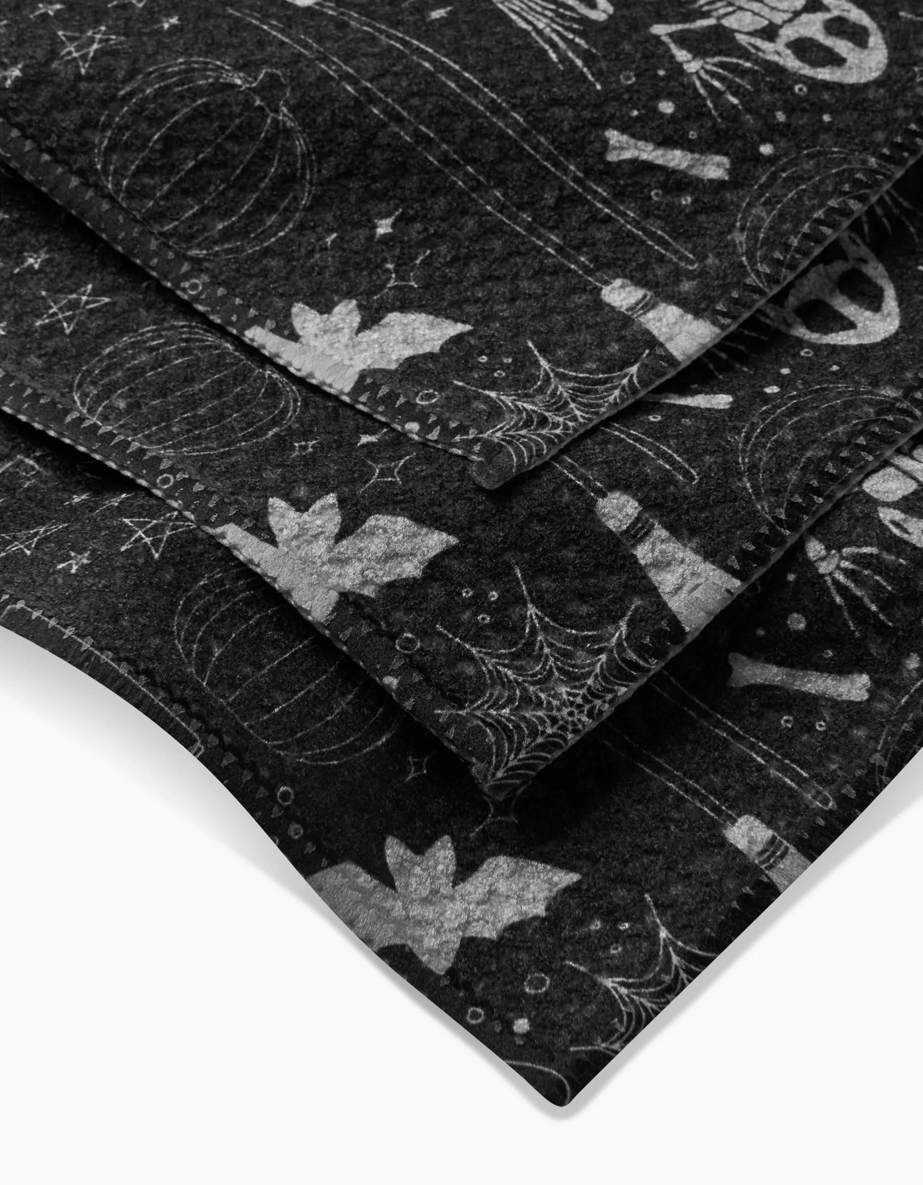Witches Brew by Rosa Kichline features layered black Geoweave dishcloths with white Halloween designs—bats, spiderwebs, pumpkins, bones, and eyeballs—super-absorbent and stylish for any spooky kitchen.