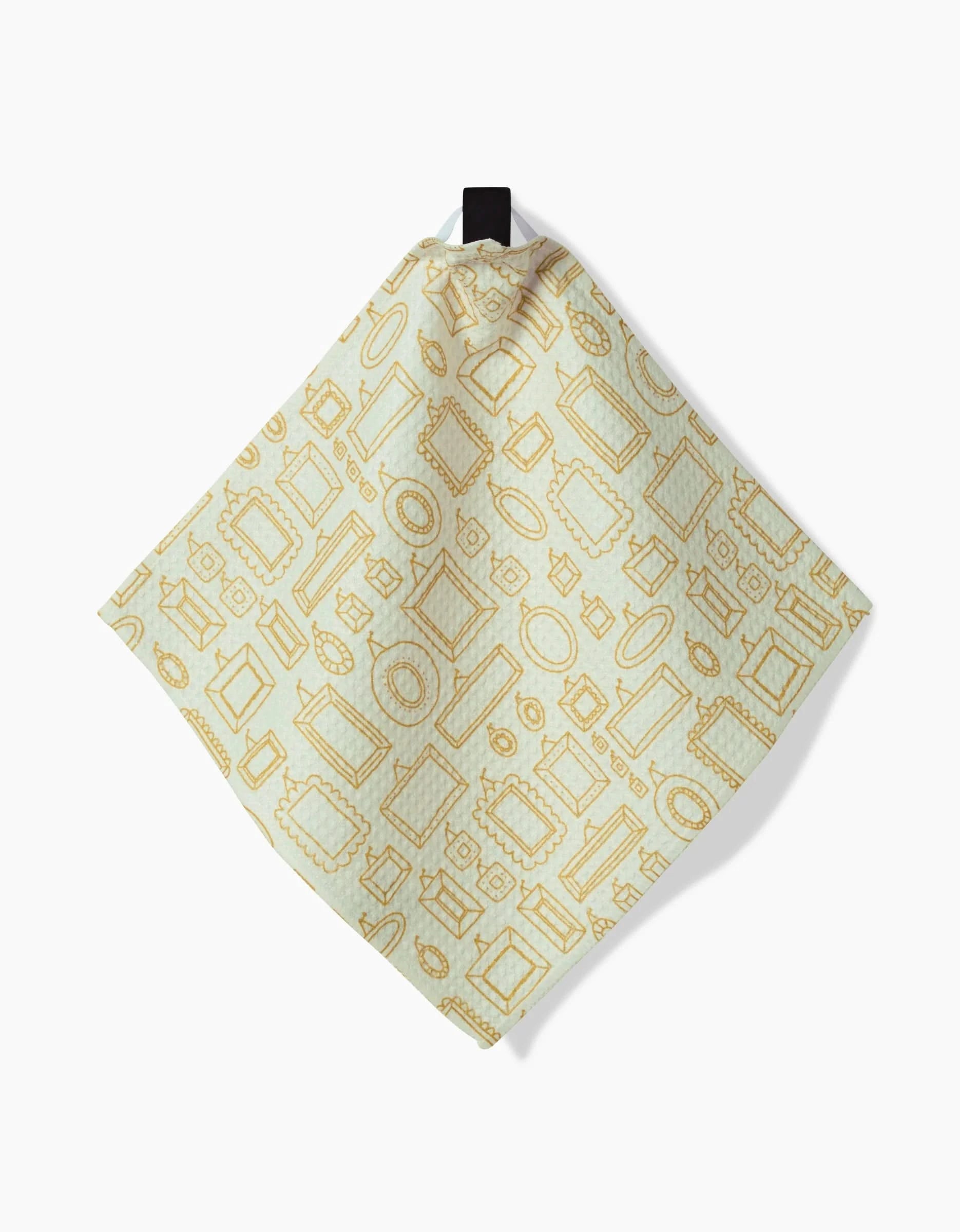The Witchy Season dishcloth by Amy MacCready is a light-colored square, hanging from a black loop. Made from recycled materials, it displays a repeating pattern of gold picture frames in assorted shapes and sizes.