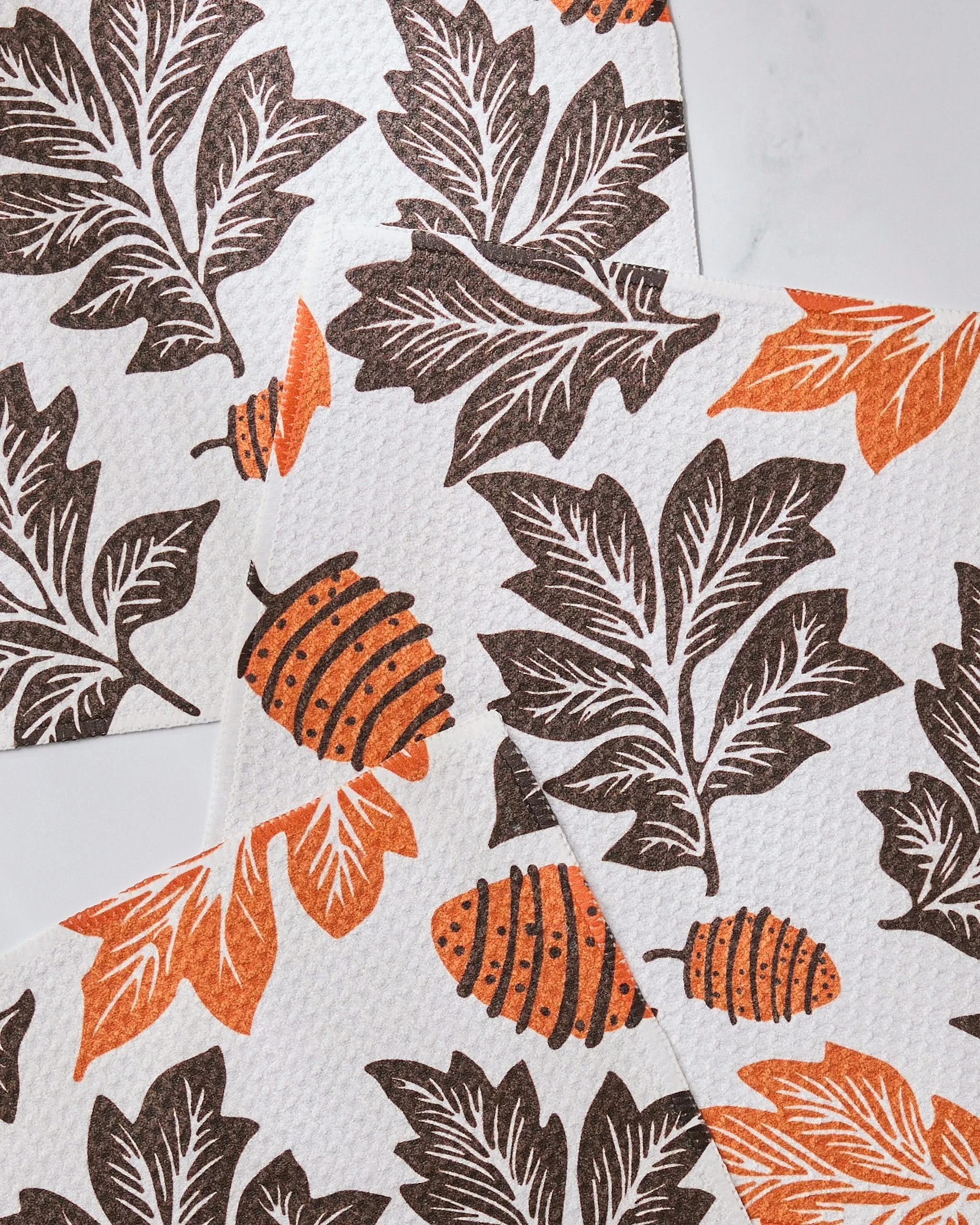 Geometrys Woodland Waltz paper towels showcase large brown and orange leaves with acorns on white, arranged in overlapping layers—crafted from recycled materials for eco-friendly cleanup.
